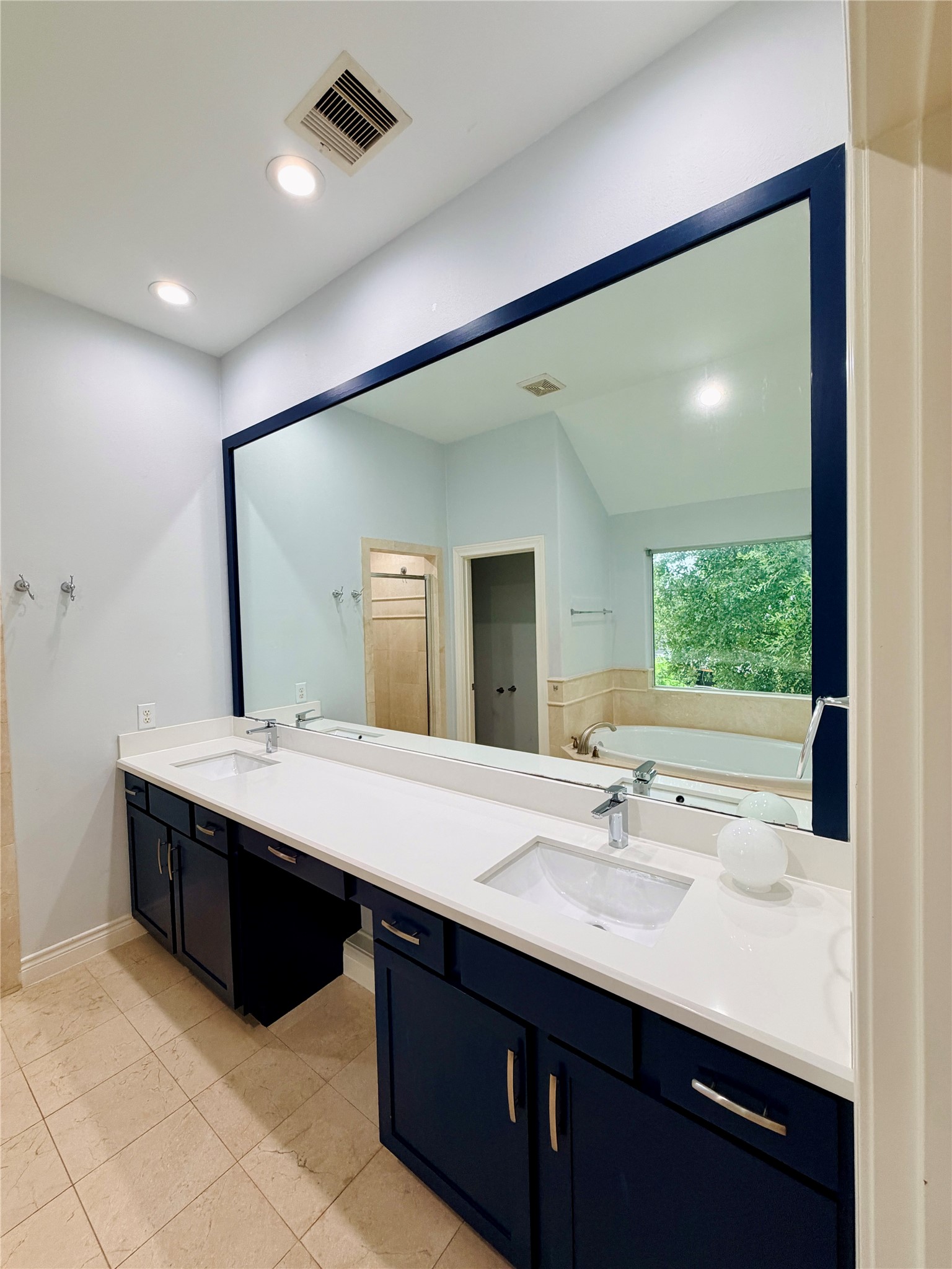 The oversized dual-sink vanity features sleek quartz countertops, modern fixtures, abundant cabinet storage, and a full-width framed mirror.