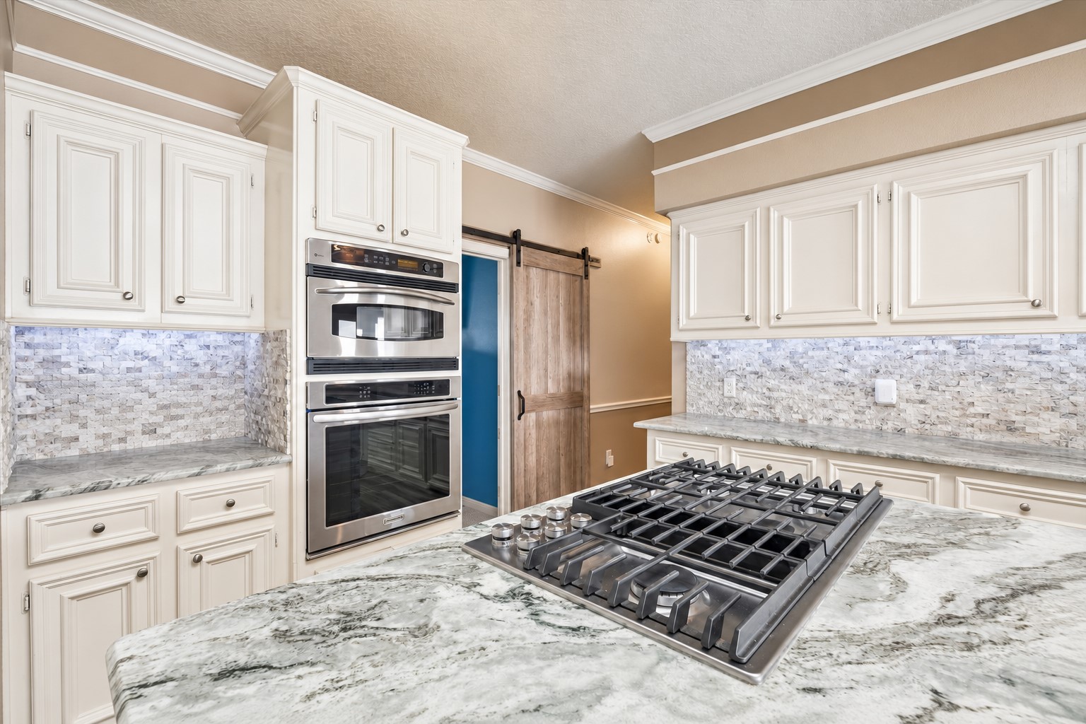 THE KITCHEN INCLUDES DOUBLE WALL OVENS, A LARGE GAS COOKTOP, GENEROUS PREP SPACE, AND A SLIDING BARN DOOR LEADING TO THE ADJOINING AREA.