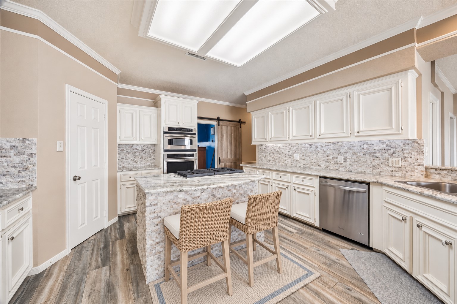 A SPACIOUS CENTER ISLAND WITH A GAS COOKTOP ANCHORS THE KITCHEN, SURROUNDED BY ABUNDANT CABINETRY, STONE COUNTERTOPS, AND STAINLESS STEEL APPLIANCES. *Virtually Staged.
