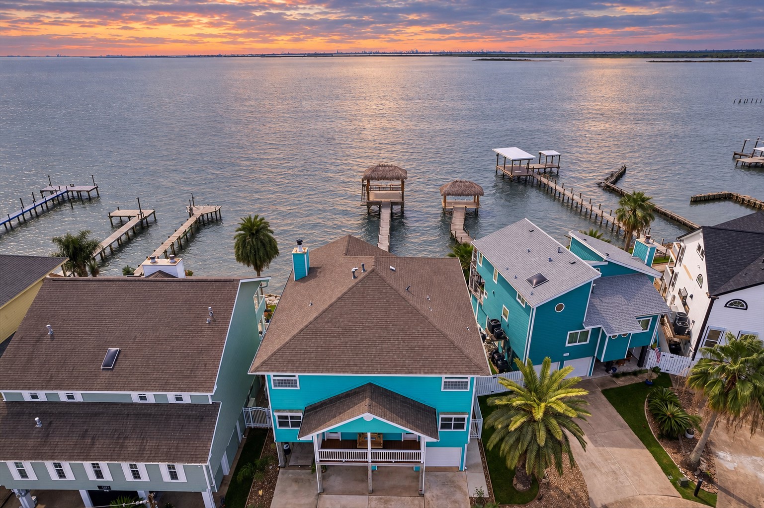 EXPANSIVE AERIAL VIEW HIGHLIGHTING THE WATERFRONT SETTING, PRIVATE PIERS, AND MULTIPLE COVERED PALAPA AREAS. THE OPEN BLUE-GRAY WATER AND DISTANT HORIZON EMPHASIZE THE PROPERTYS DIRECT BAY ACCESS.