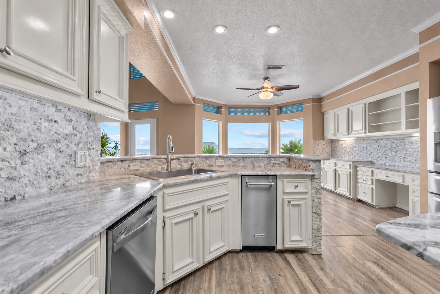 EXPANSIVE KITCHEN WITH ABUNDANT CABINETRY, GENEROUS COUNTER SPACE, STAINLESS STEEL APPLIANCES, AND WATER VIEWS THROUGH MULTIPLE WINDOWS.