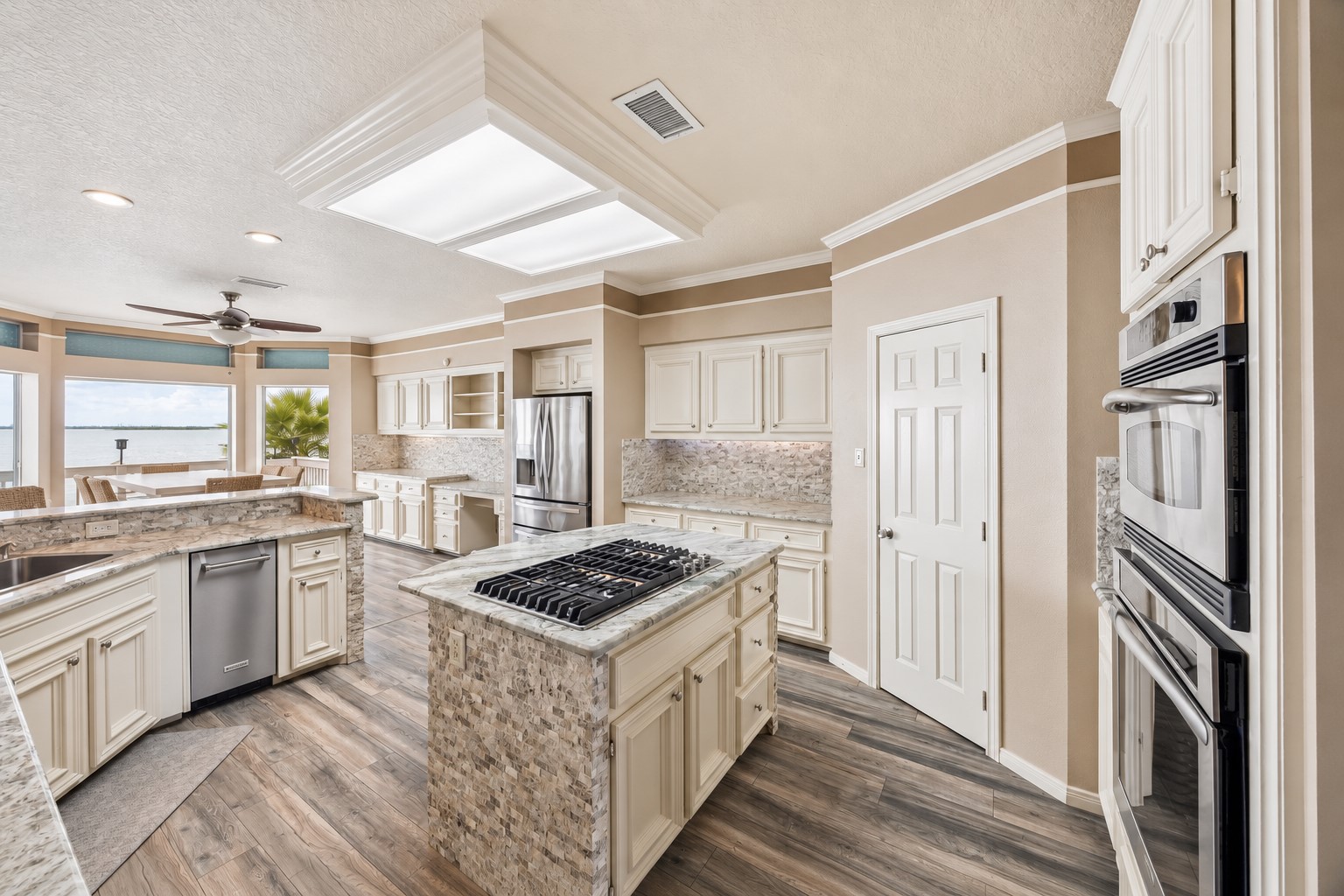 THIS WIDE KITCHEN VIEW HIGHLIGHTS MULTIPLE WORK ZONES, SUBSTANTIAL STORAGE, AND LARGE WINDOWS SHOWCASING THE WATERFRONT SETTING.
