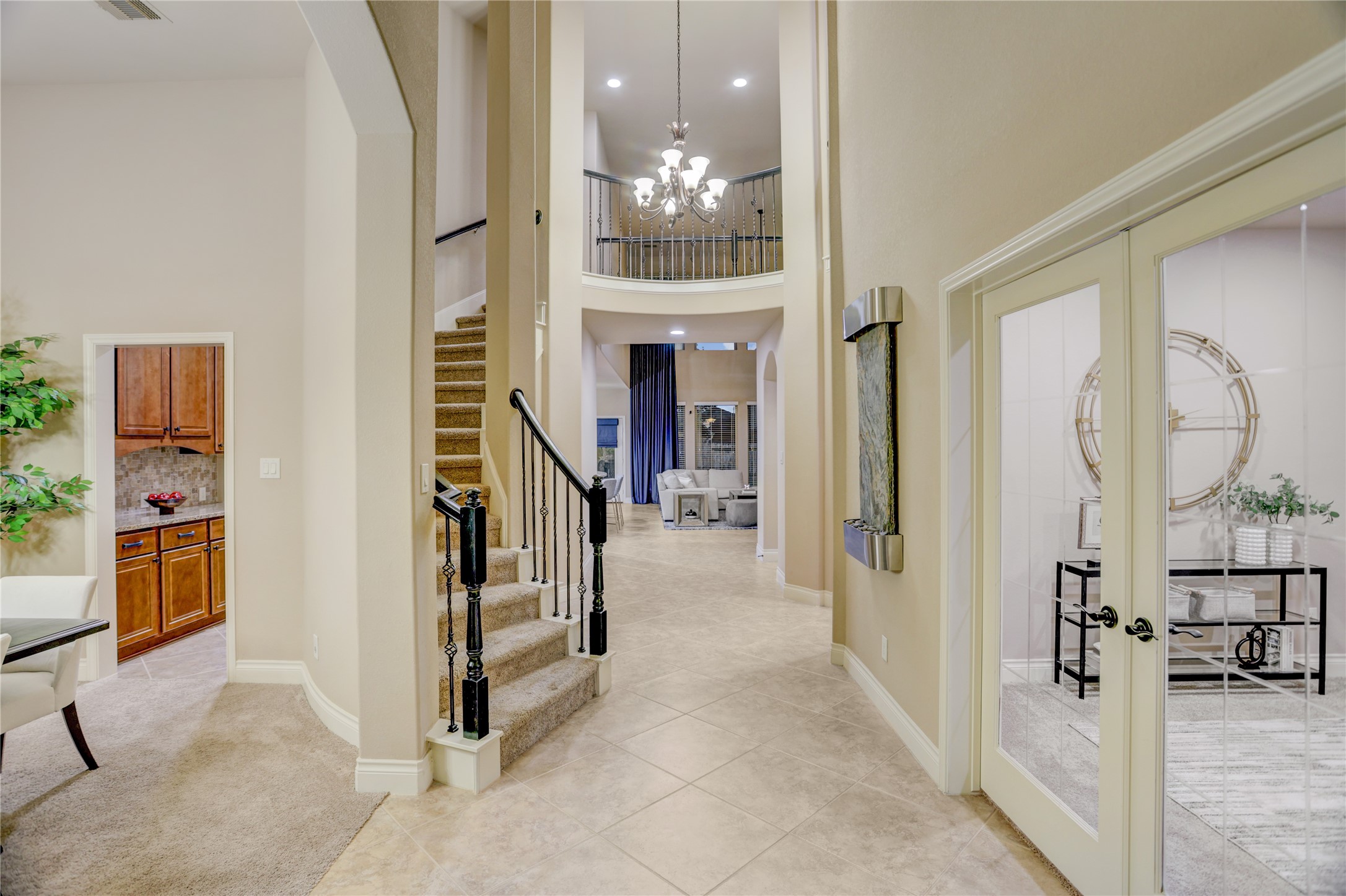 Step into a grand two-story foyer featuring soaring ceilings, elegant tile flooring, a sweeping staircase with wrought-iron balusters, and a stunning overlook from the second floor. French doors open to a private home office, while the formal dining room offers the perfect space for entertaining. The entry sets the tone for the home's spacious design.