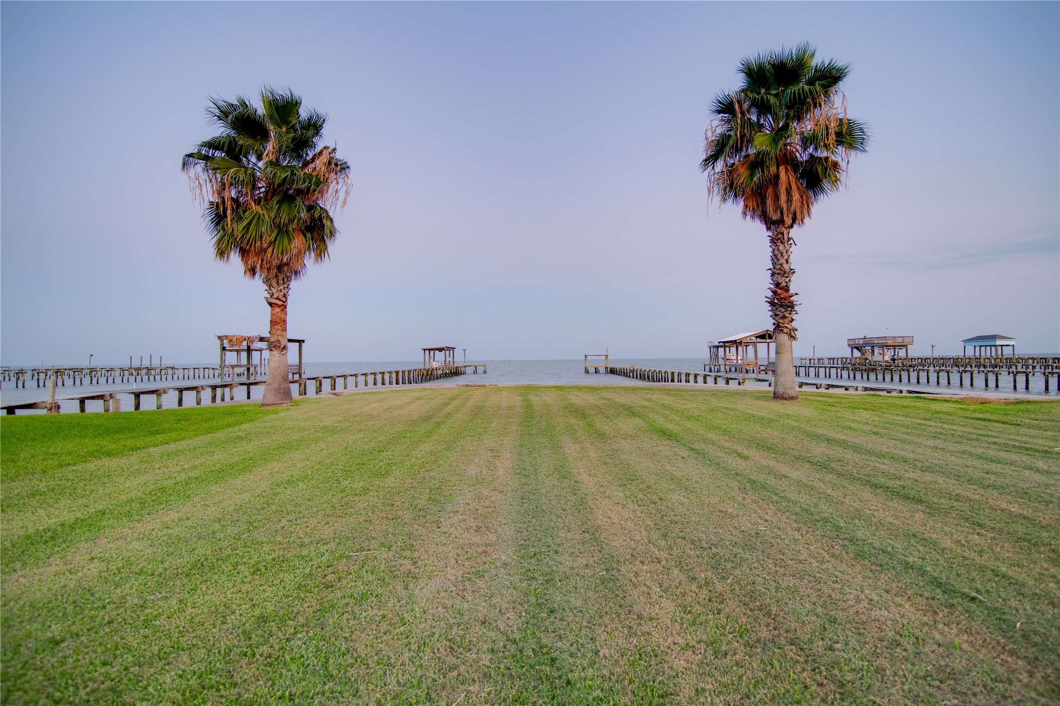 How about transforming this large grassy space between the deck and the ocean into a versatile outdoor haven. Possibilities include creating a private garden with tropical or coastal plants, adding a fire pit area for evening gatherings, setting up a play area for children or pets, or installing an outdoor dining and lounge space to enjoy meals with panoramic water views. The open lawn also provides ample room for a pool, putting green, or other recreational features to enhance waterfront living.