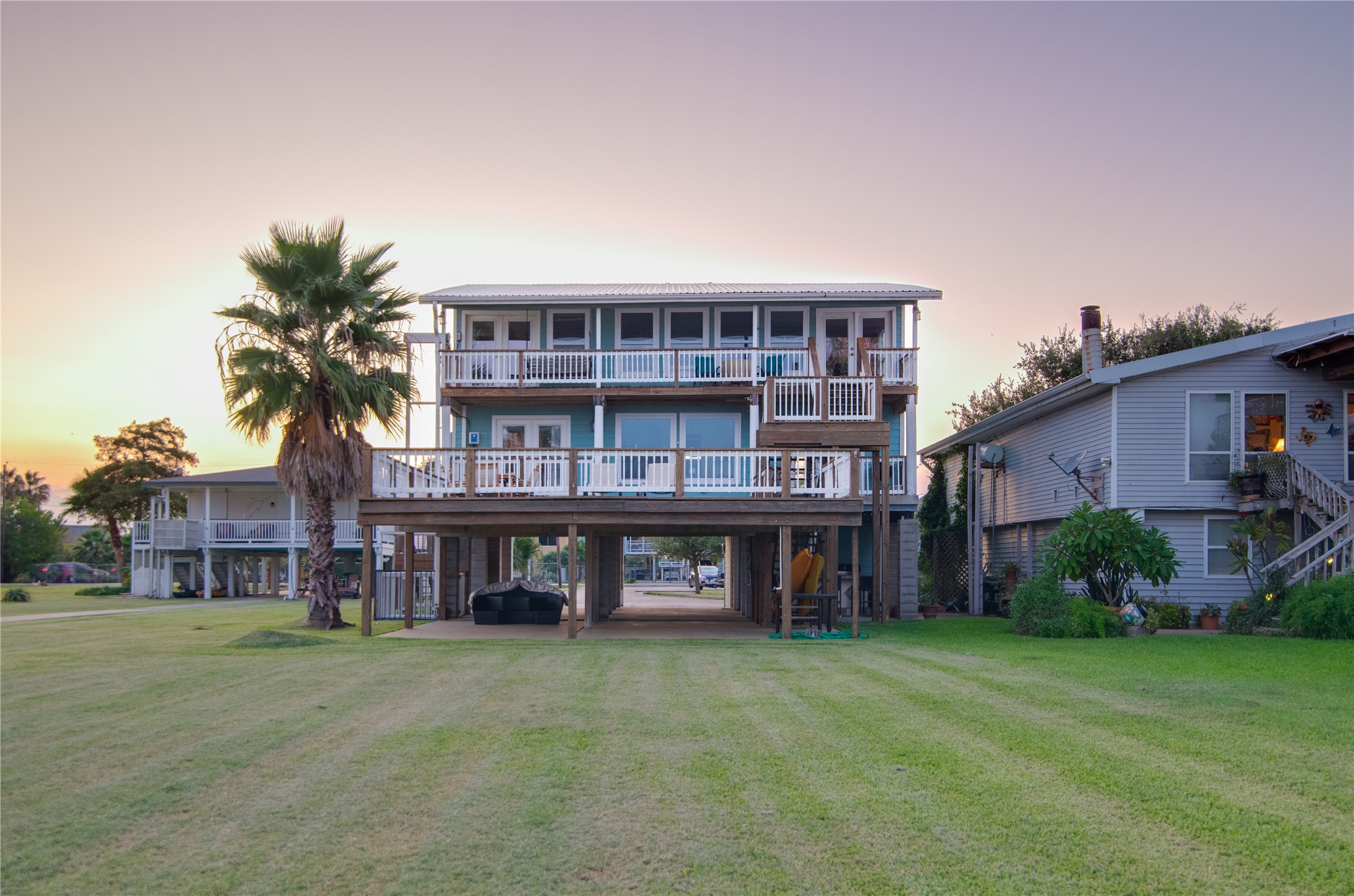From the bay, the home presents a stunning waterfront view, showcasing a spacious balcony and an expansive deck that stretch across the rear of the house. Large windows reflect the water and invite natural light inside, hinting at the bright, airy interiors beyond. The combination of outdoor living spaces and panoramic windows creates a striking, inviting faade that perfectly complements the tranquil bay setting.
