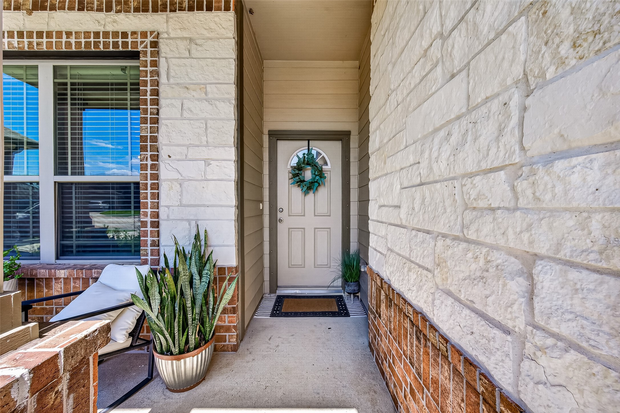 Charming entryway with stone and brick accents, featuring a welcoming front door adorned with a decorative wreath and surrounded by lush potted plants. Charming entryway with stone and brick accents, featuring a welcoming front door adorned with a decorative wreath and surrounded by lush potted plants.