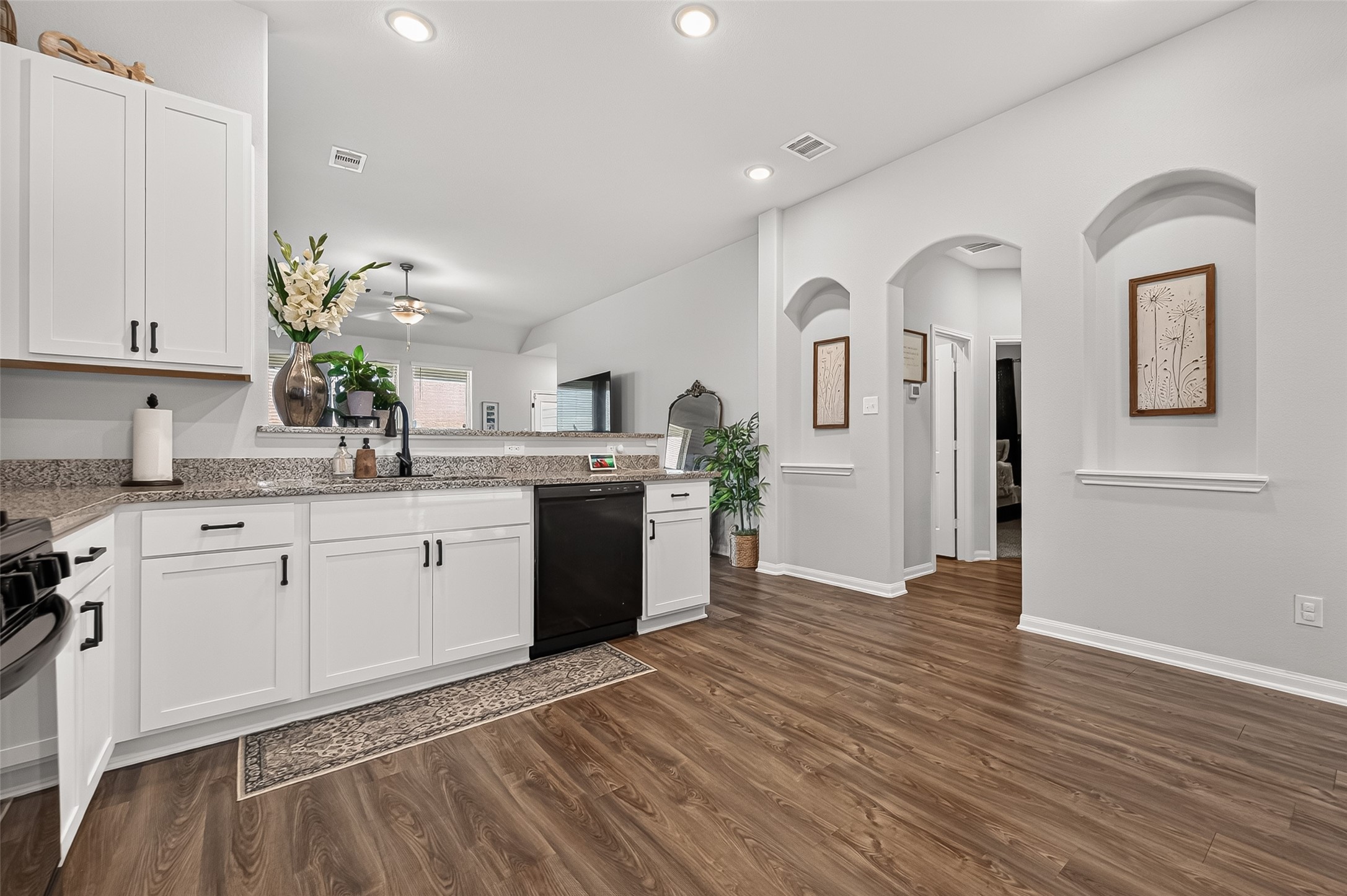 Spacious kitchen with elegant white cabinetry, granite countertops, and modern black appliances, complemented by warm wood flooring and stylish archways.