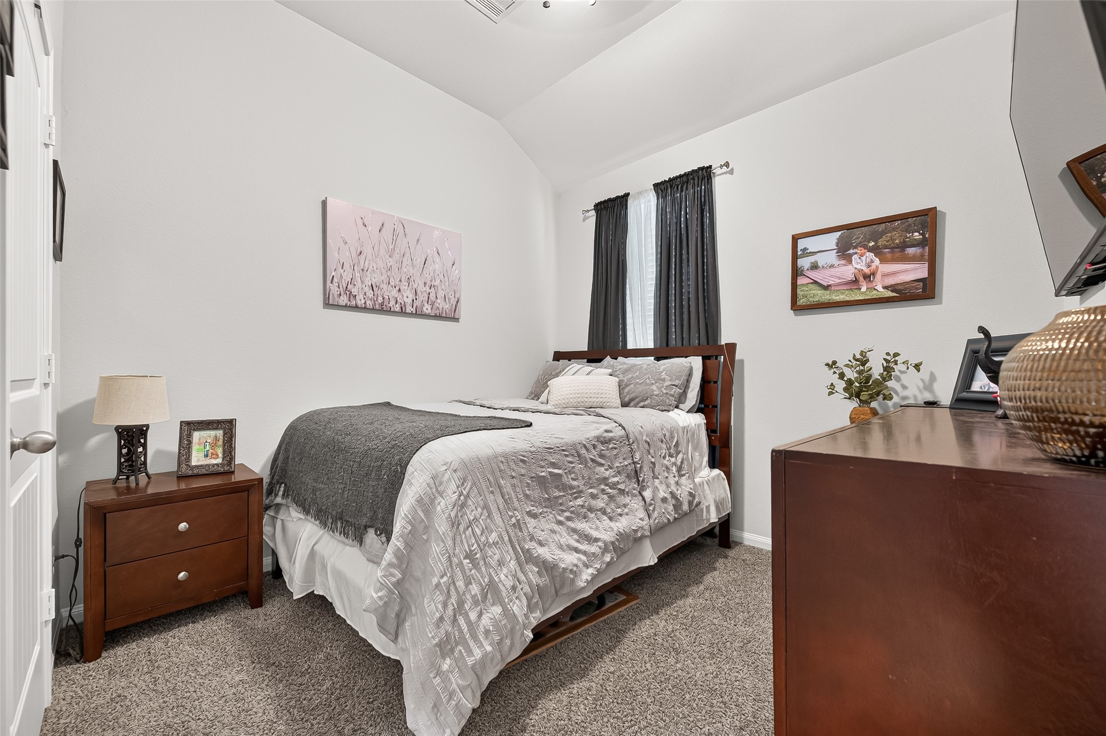 Cozy bedroom with plush carpeting, featuring a comfortable bed and stylish dark wood furniture. Natural light filters through the window, complementing the room's soothing color palette.