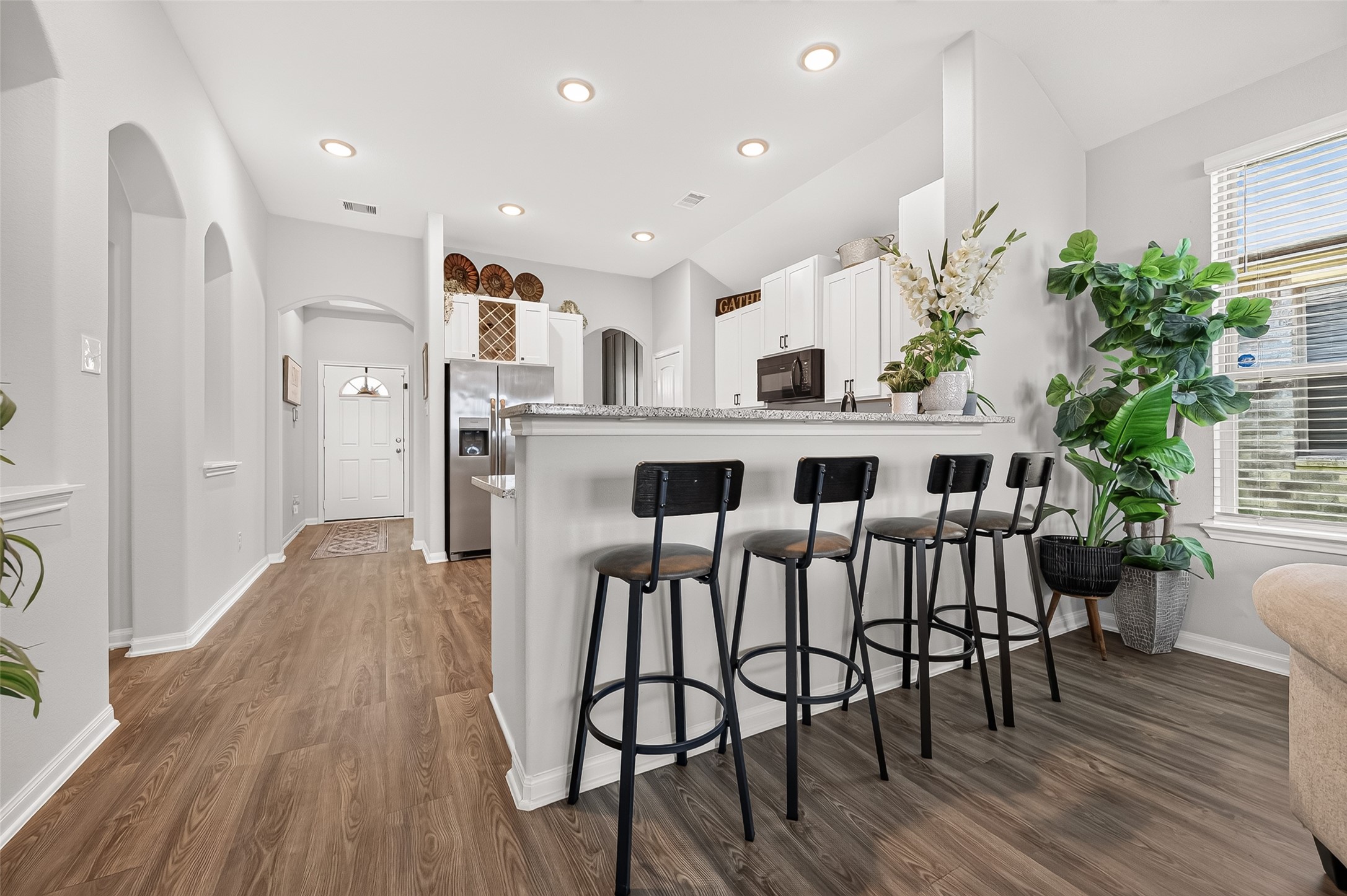 Modern kitchen features a spacious breakfast bar with sleek black stools, complemented by beautiful hardwood floors and abundant natural light.
