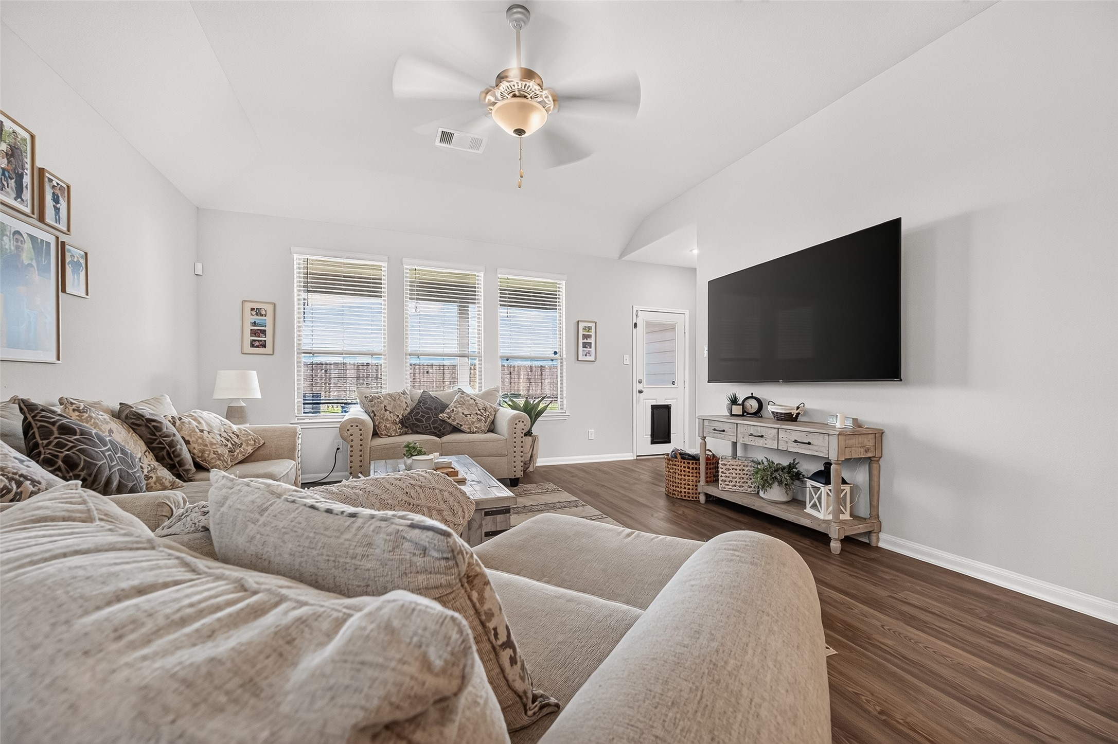 Spacious living room with abundant natural light, featuring cozy seating, a large TV, and stylish decor on wood flooring.