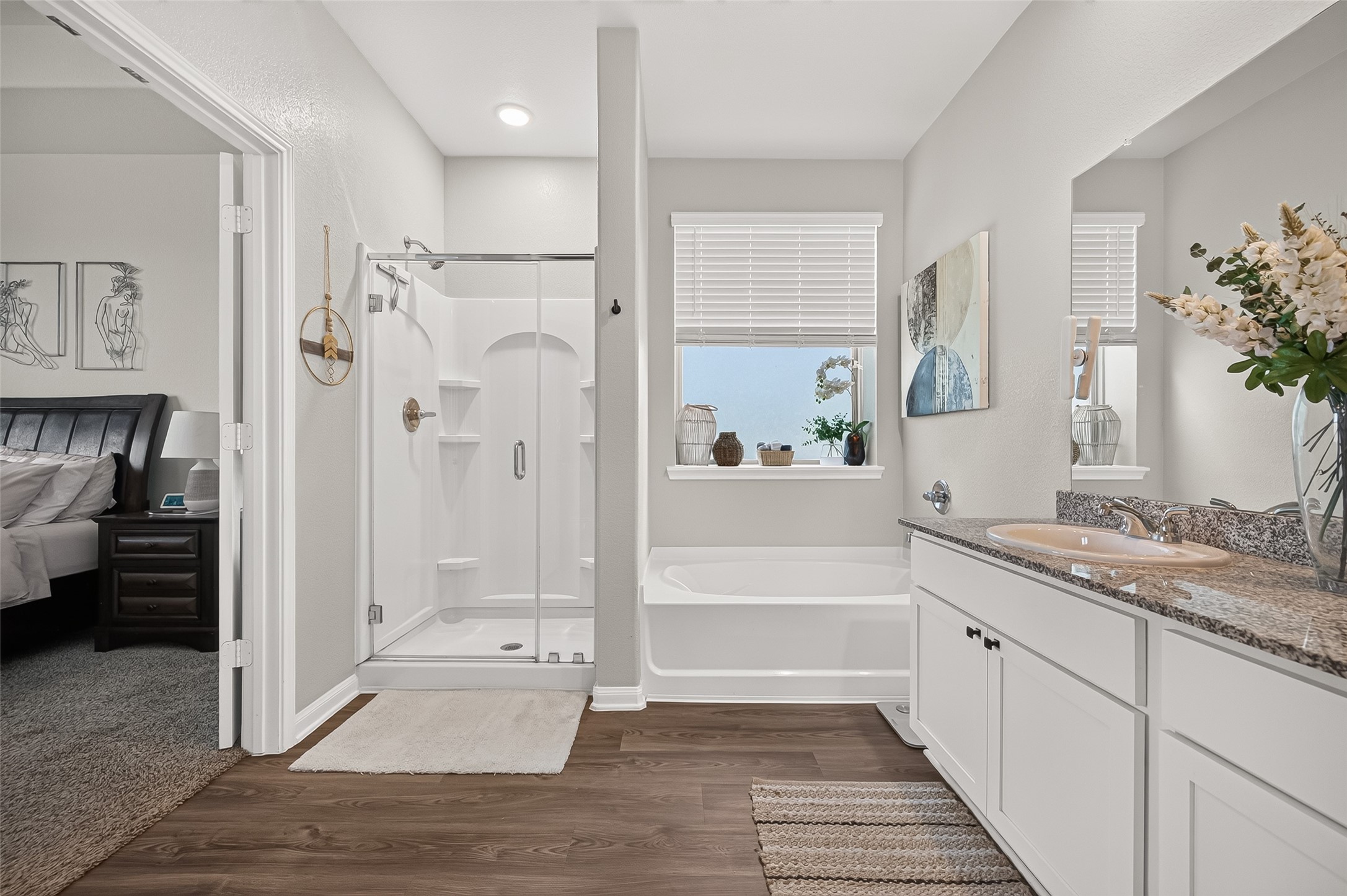 Bright and modern bathroom featuring a spacious glass-enclosed shower, cozy bathtub, and elegant granite countertop with dual sinks, seamlessly connecting to the bedroom.