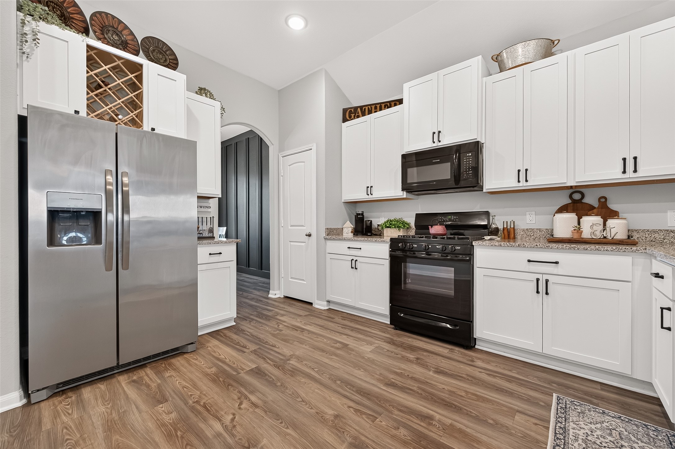 The kitchen features sleek stainless steel appliances, elegant white cabinetry with black hardware, and warm wood flooring, creating a modern and inviting space.