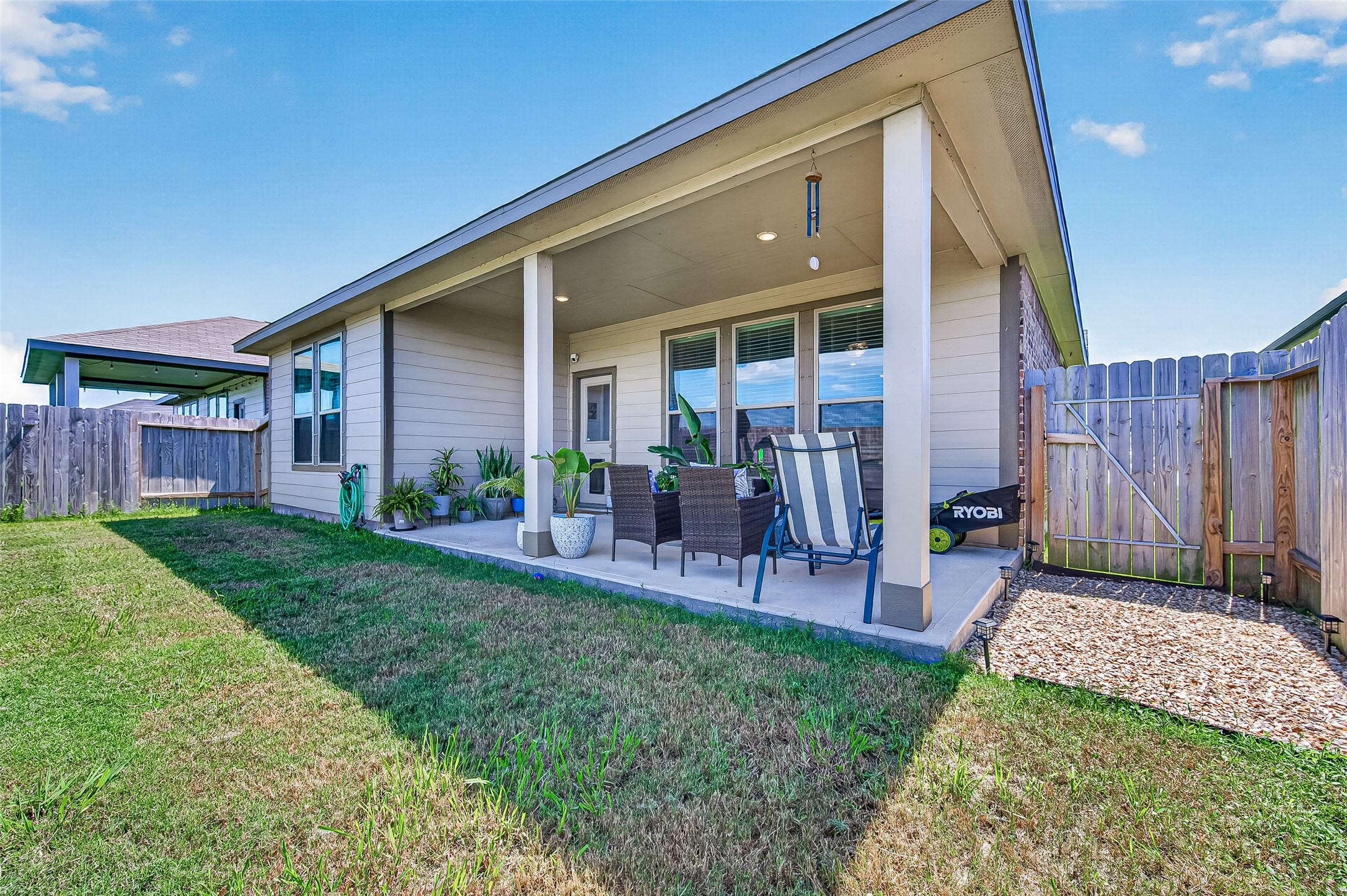 Charming covered patio with cozy seating area, perfect for outdoor relaxation, set within a fenced backyard offering privacy and tranquility.