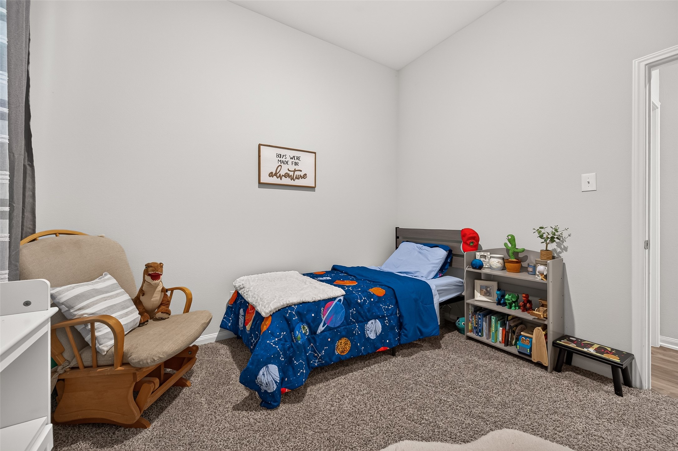 Cozy children's bedroom featuring a space-themed bedspread, plush carpeting, and a charming reading nook with a rocking chair.