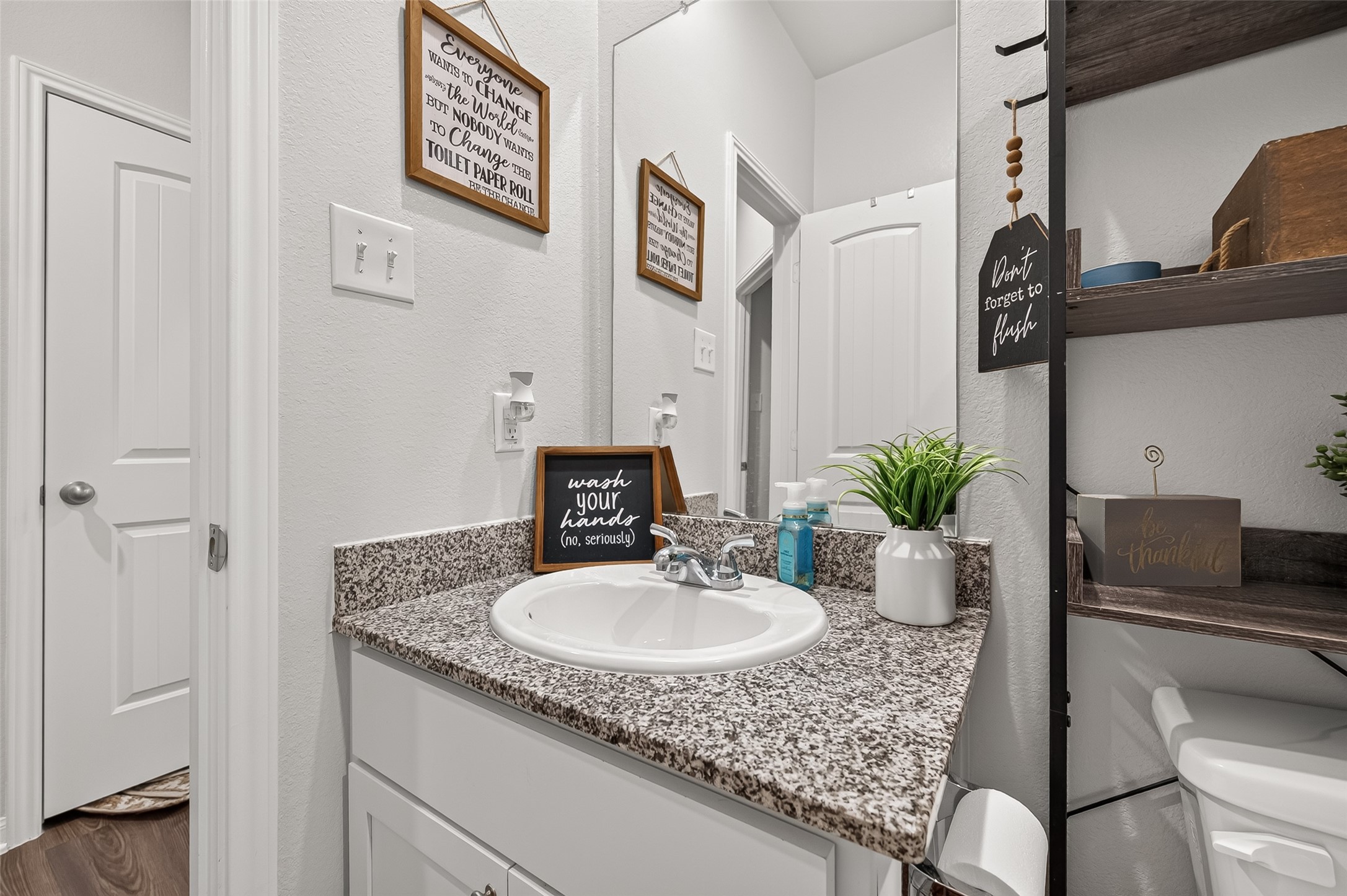 Charming bathroom with modern granite countertop, stylish shelving, and a cozy decor touch, perfect for daily convenience.