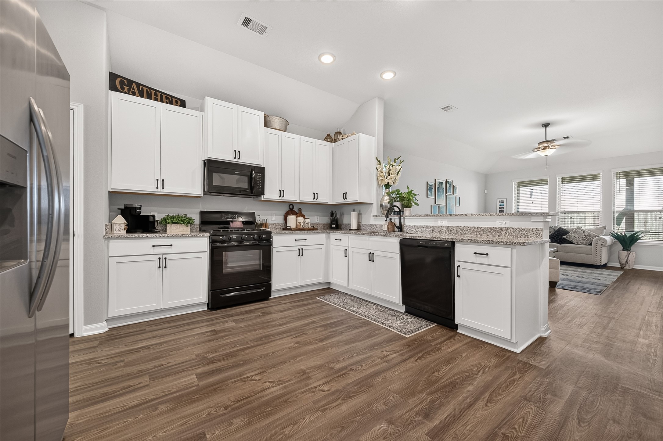 Spacious kitchen with modern appliances, elegant white cabinetry, and sleek granite countertops, seamlessly flowing into a bright, inviting living area.
