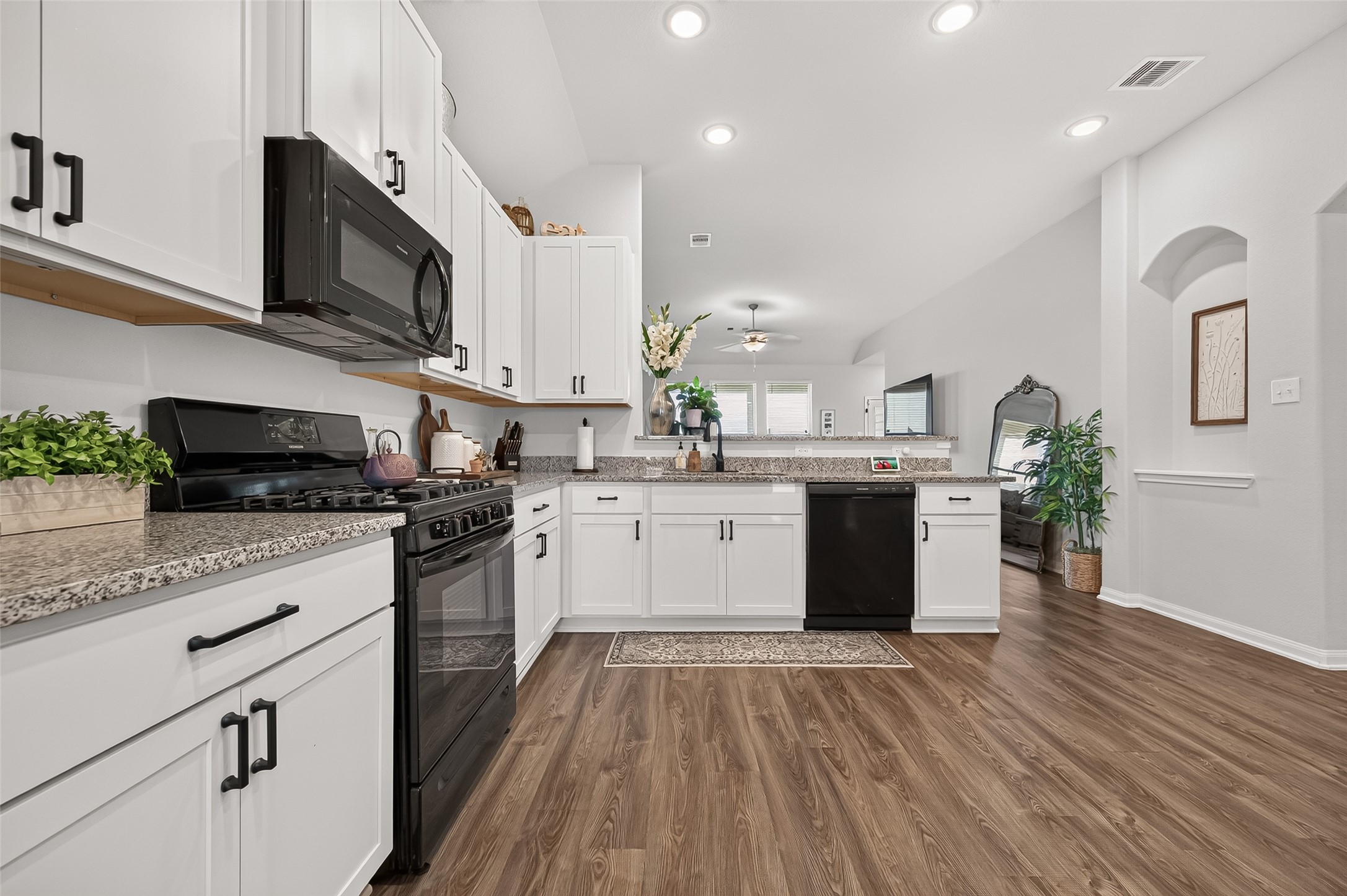 A spacious kitchen with modern appliances, sleek granite countertops, and elegant white cabinetry, seamlessly connecting to a cozy living area with warm wood flooring.