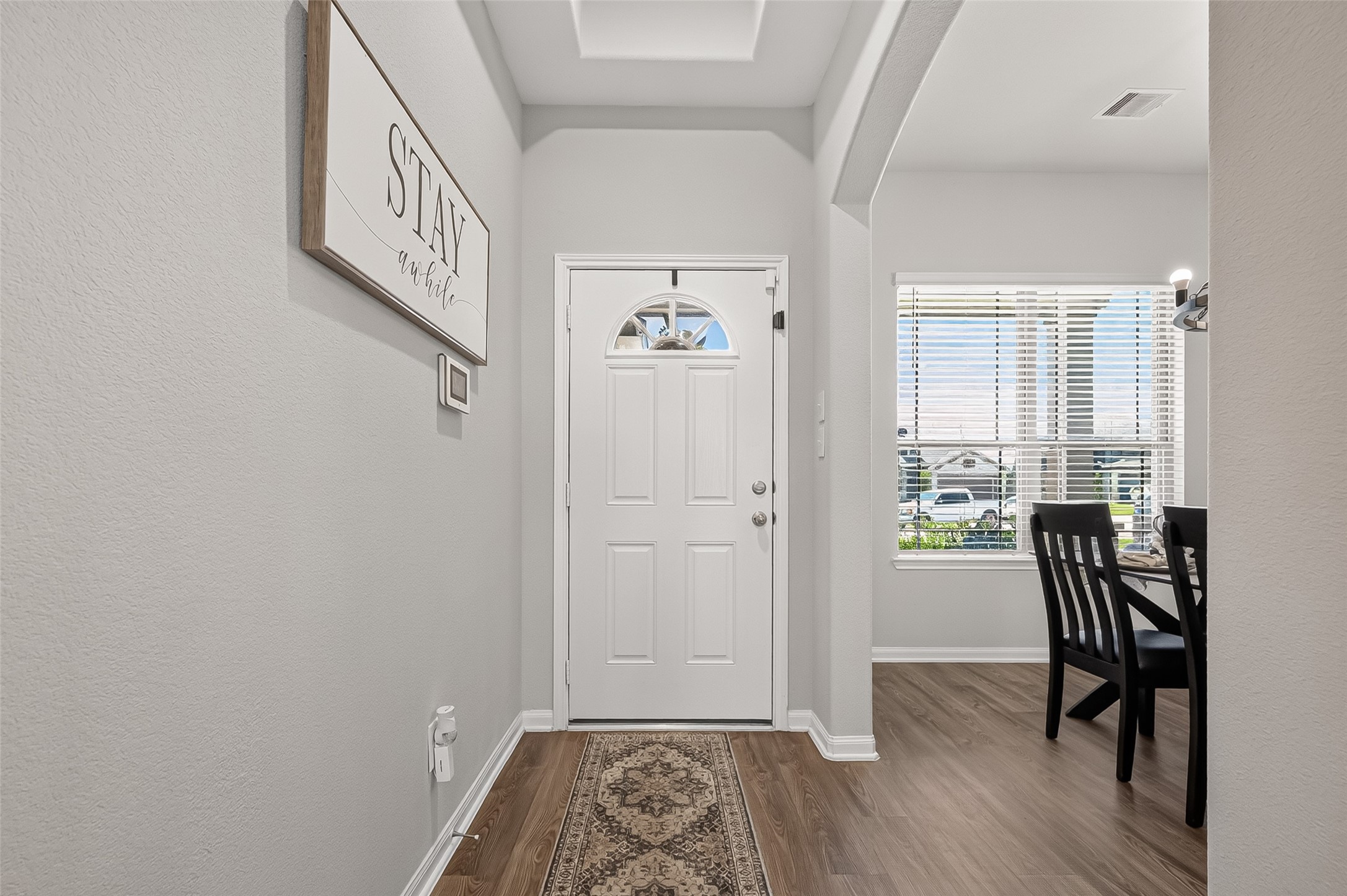 Inviting entryway featuring a white front door, elegant wood flooring, and an arched opening leading to a bright dining area with large windows. Inviting entryway featuring a white front door, elegant wood flooring, and an arched opening leading to a bright dining area with large windows.