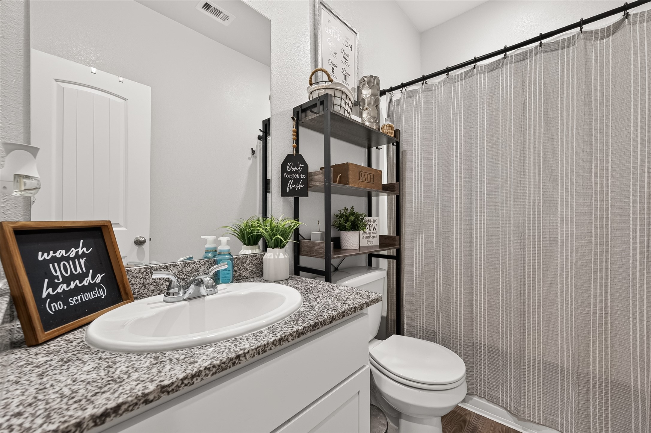 Charming bathroom with modern fixtures, featuring a sleek granite countertop, ample shelving for storage, and a stylish shower curtain for a cozy touch.