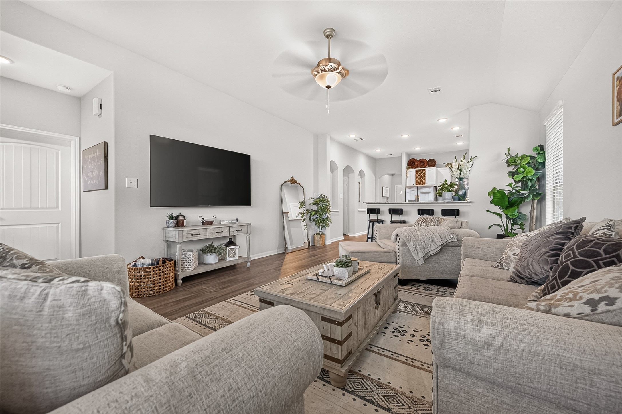 Spacious living area with cozy gray sofas and a stylish coffee table, leading to an open kitchen with bar seating. Natural light and elegant decor create a warm, inviting ambiance.
