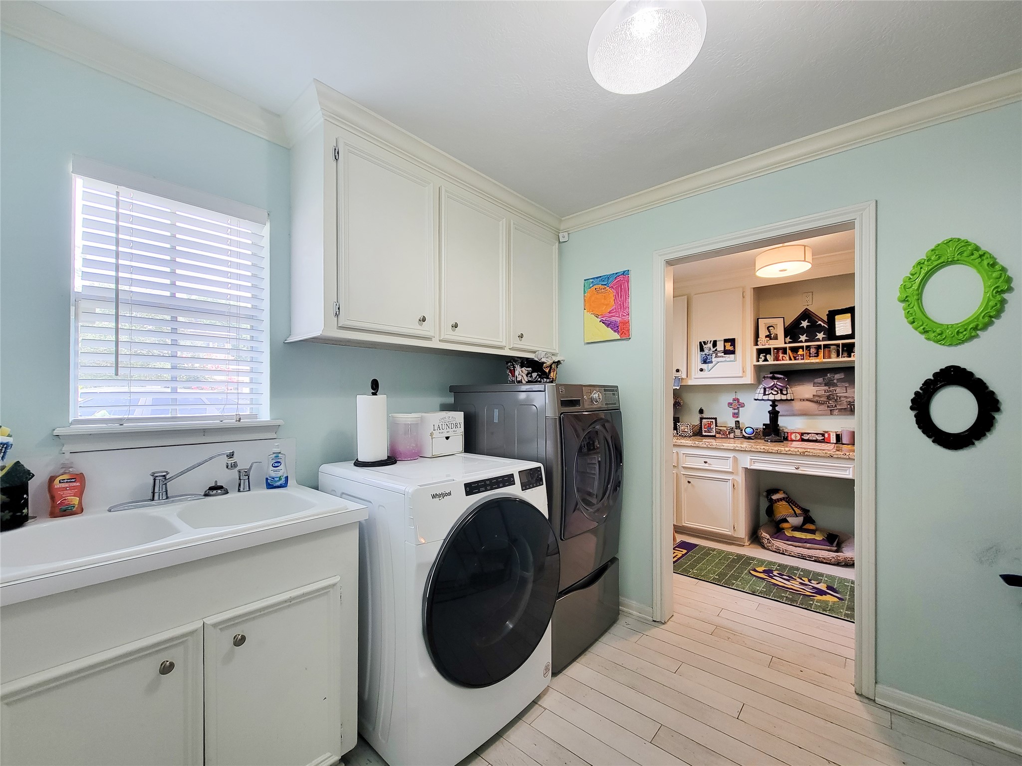 This photo shows a bright, functional laundry room with modern appliances, ample cabinet storage, and a sink. The adjacent area appears to be a cozy workspace or pet area, enhancing utility and convenience.