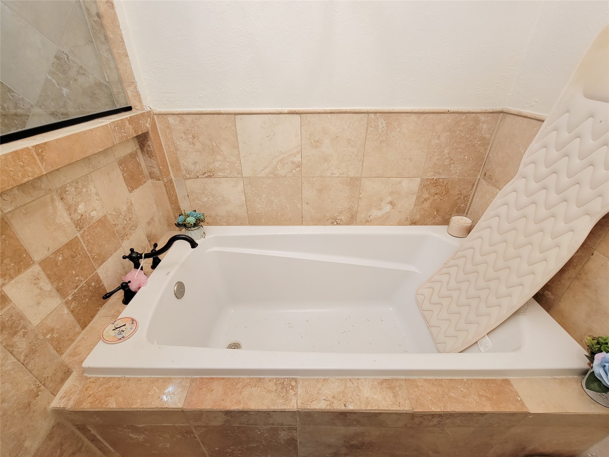 This bathroom features a cozy bathtub with beige tile surround, accented with decorative fixtures and a comfortable bath mat.