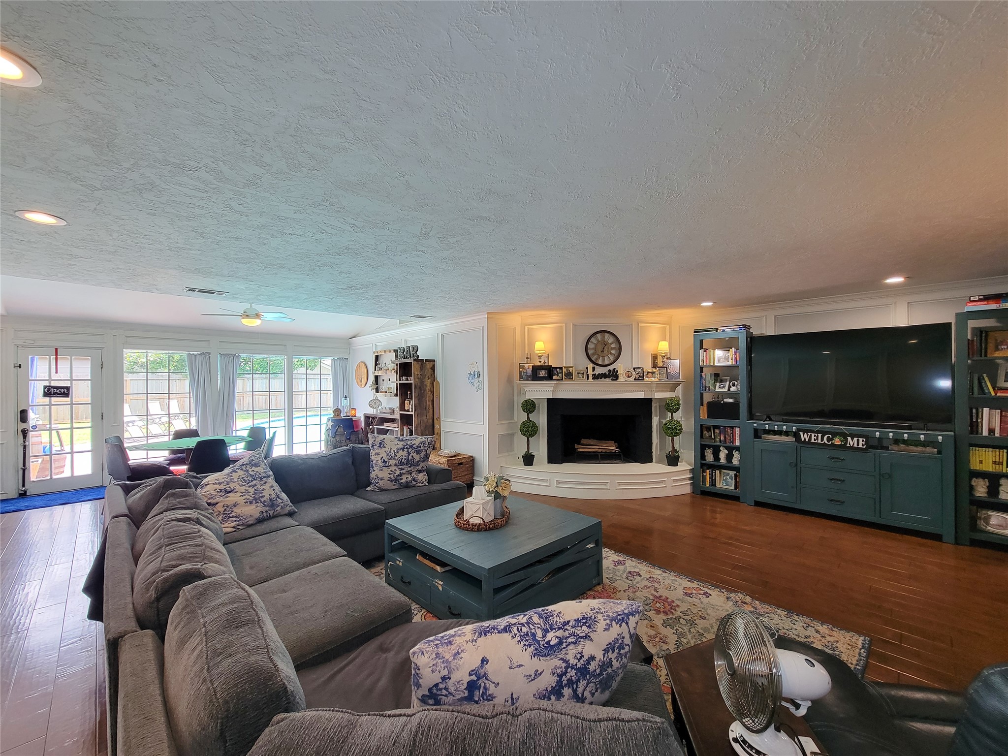This spacious living room features a cozy fireplace, built-in shelving, and a large entertainment area. Ample natural light floods through the glass doors leading to the backyard. The seating area is inviting, making it perfect for family gatherings.