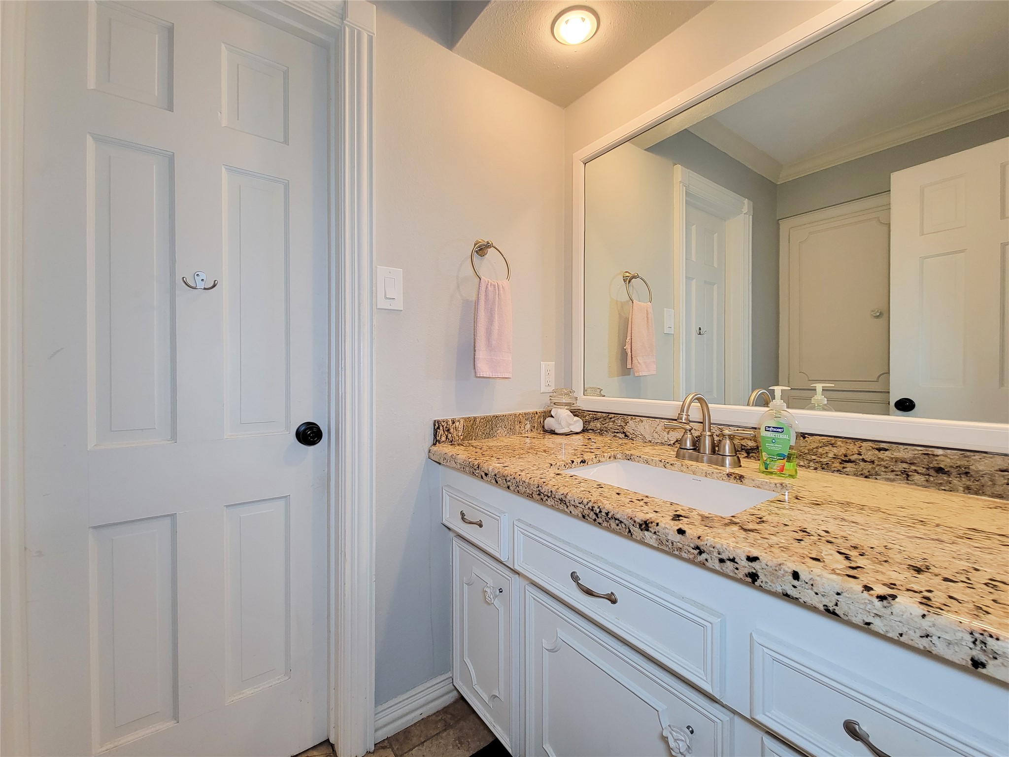 This bathroom features a granite countertop with a single sink, white cabinetry, and a large mirror. The neutral tones and simple decor create a clean, inviting atmosphere.