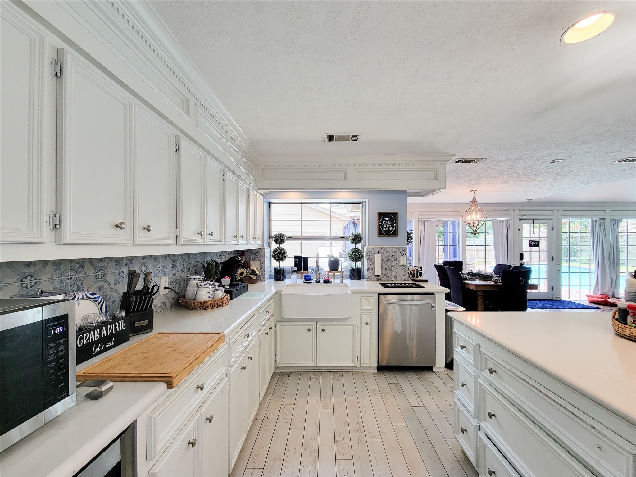 Bright and spacious kitchen with elegant white cabinetry, a farmhouse sink, and modern appliances. The open layout flows into a dining area with large windows offering a view of the pool.
