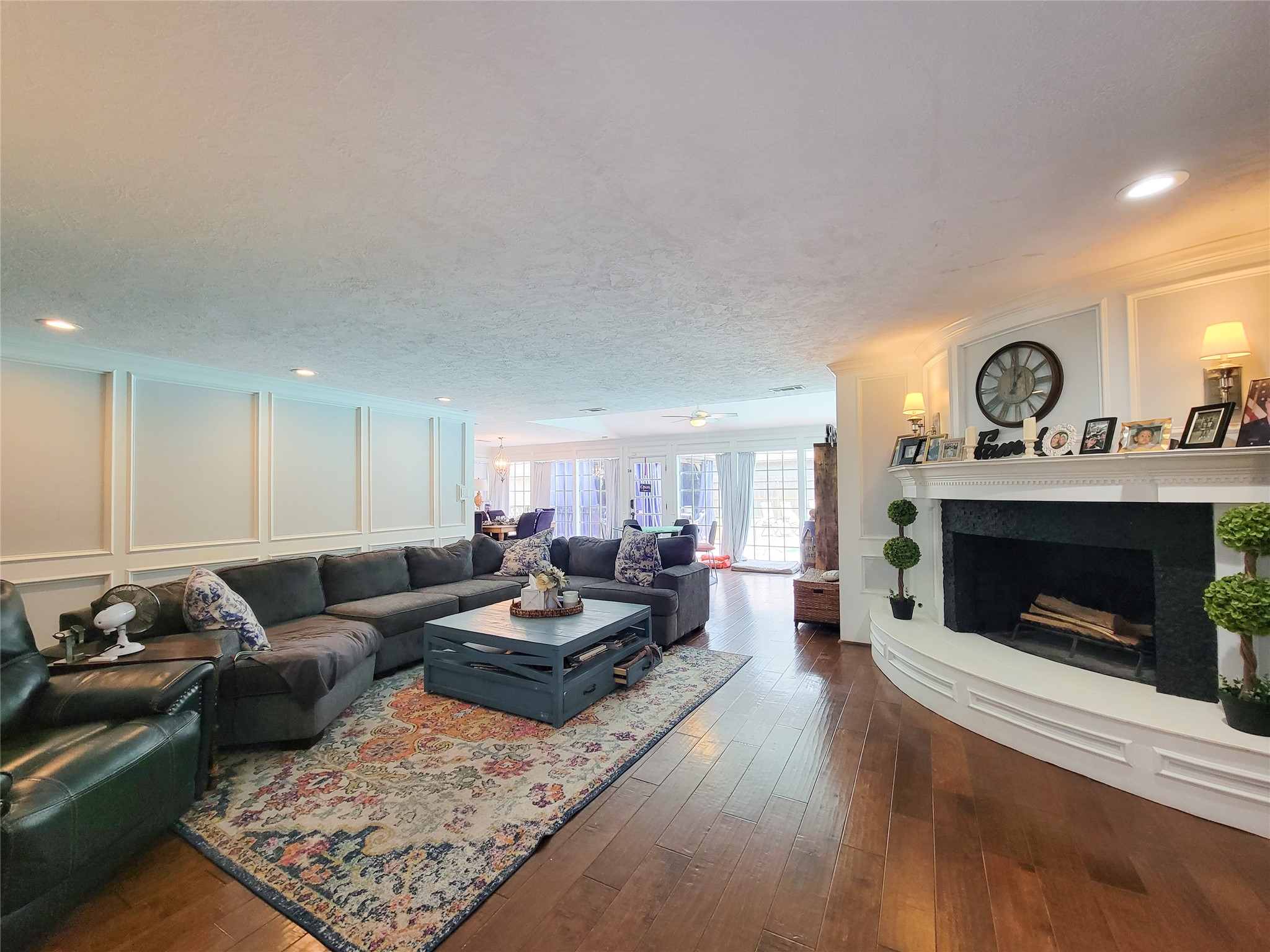 This spacious living room features elegant wood flooring, a cozy fireplace with a decorative mantel, and ample natural light from large windows. The room is accented by a stylish sectional sofa and a large area rug, offering a warm and inviting atmosphere for relaxation and entertaining.
