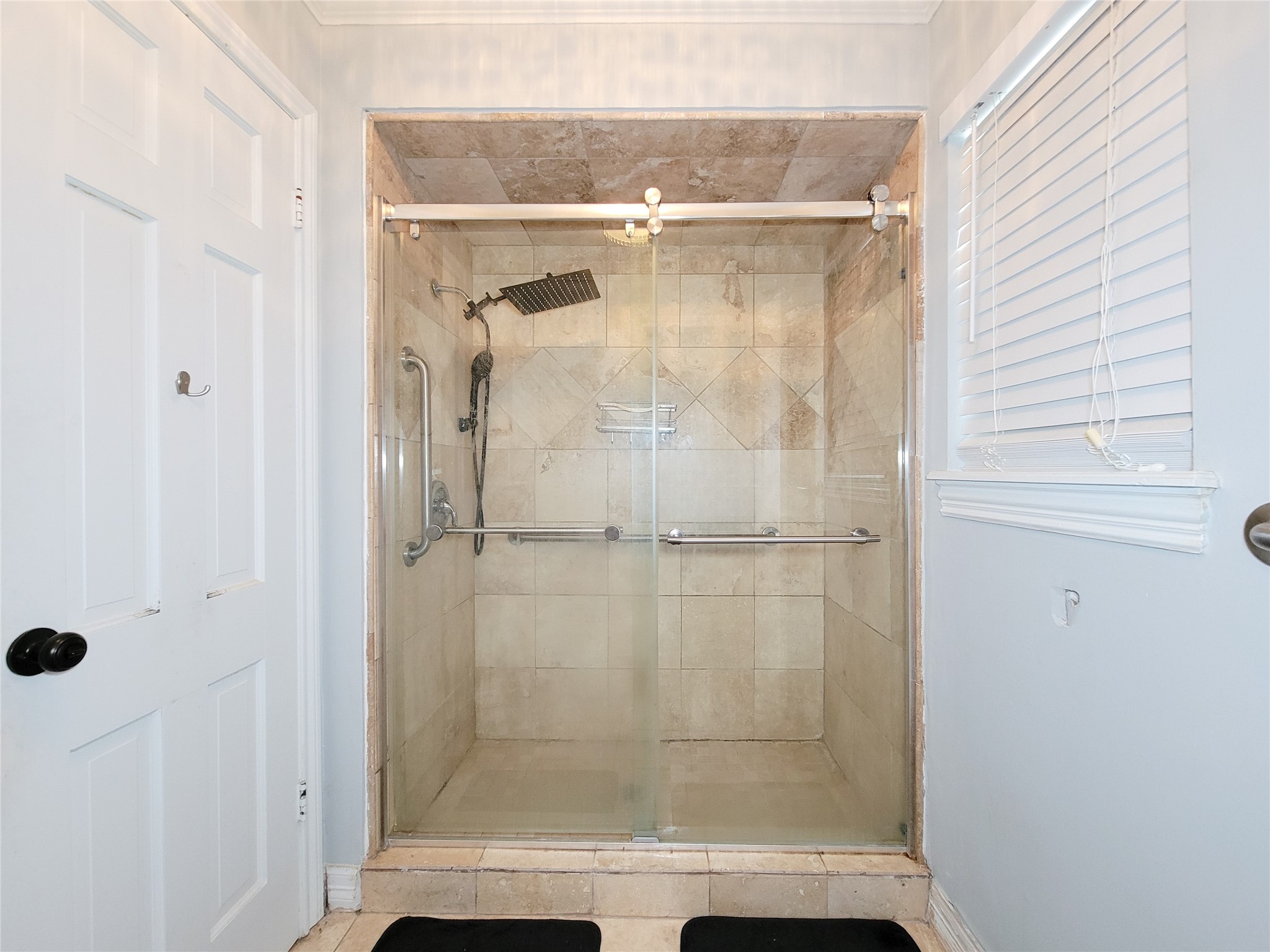 This bathroom features a spacious walk-in shower with a glass door, tiled walls and ceiling, and a modern rainfall showerhead. It includes a built-in bench and grab bars for convenience, with a window providing natural light.