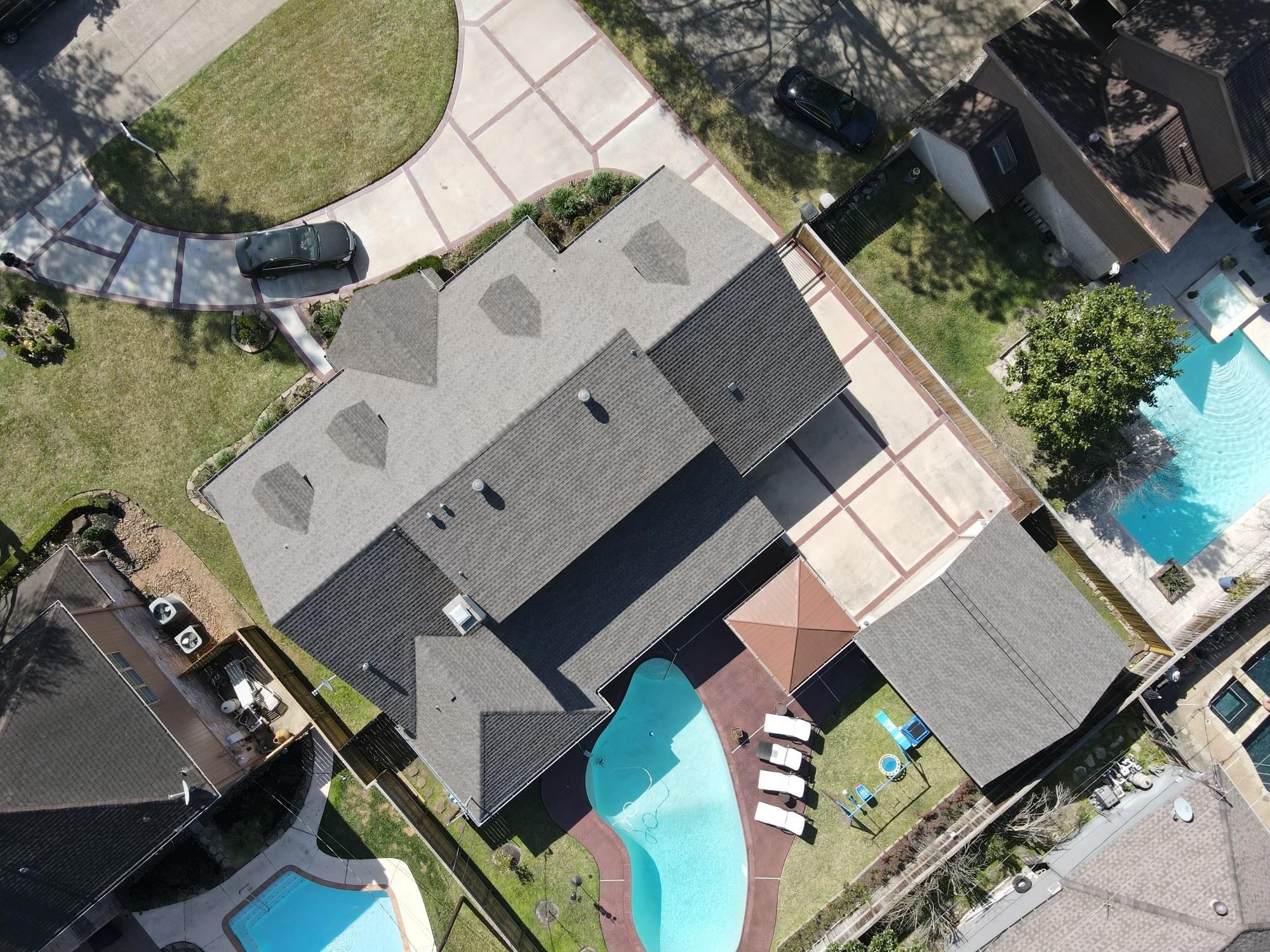 This aerial photo showcases a spacious home with a large driveway, a well-maintained yard, and a private backyard featuring a swimming pool and patio area.