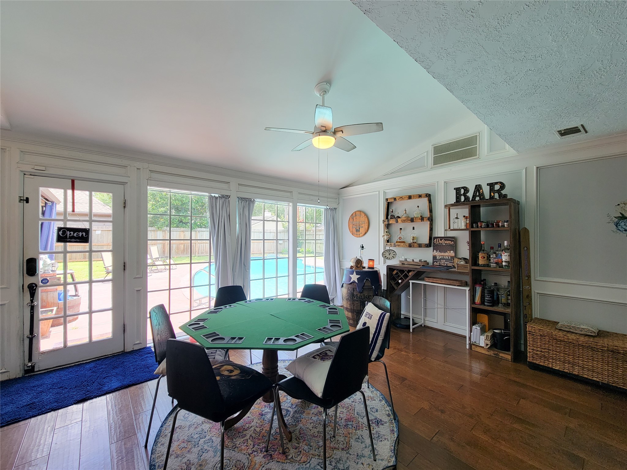 This room features a cozy entertainment area with wooden flooring and a built-in bar. Large windows and French doors offer abundant natural light and a view of the pool, creating a perfect space for gatherings and relaxation.