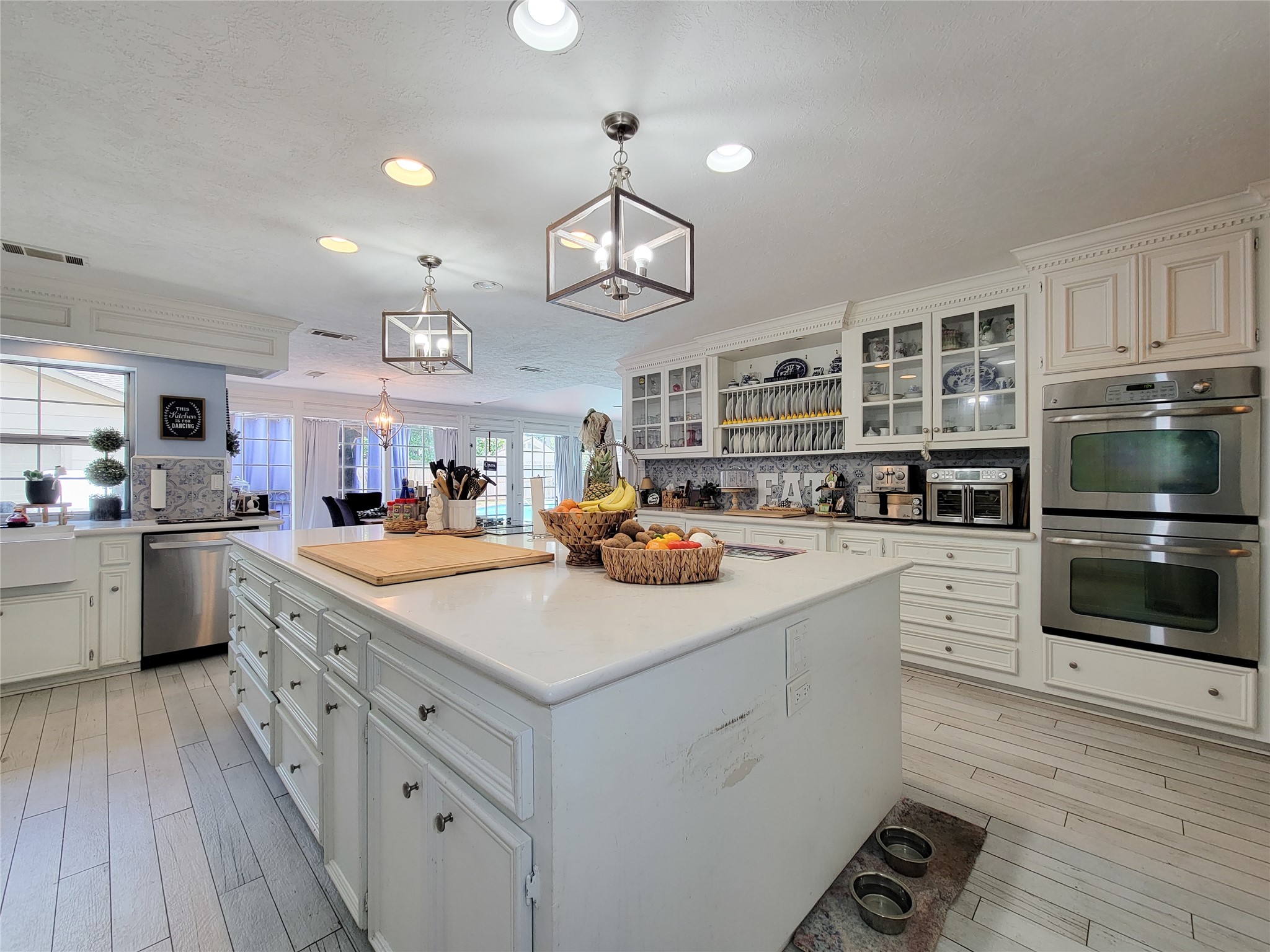 This spacious kitchen features elegant white cabinetry, modern stainless steel appliances, and a large island with ample counter space. It offers abundant natural light and a cozy, inviting atmosphere, perfect for both cooking and entertaining.