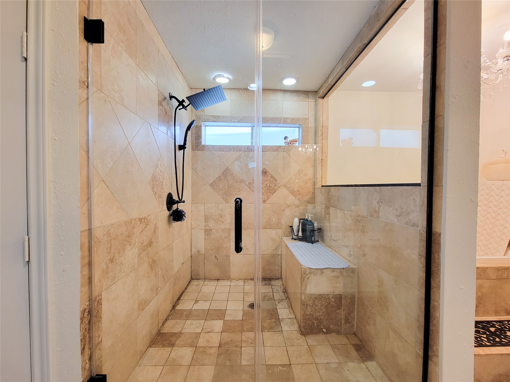 This photo showcases a spacious walk-in shower with elegant beige tilework, a rainfall showerhead, and a built-in bench. The glass enclosure adds a modern touch, complemented by ample natural light from a small window. This photo showcases a spacious walk-in shower with elegant beige tilework, a rainfall showerhead, and a built-in bench. The glass enclosure adds a modern touch, complemented by ample natural light from a small window.