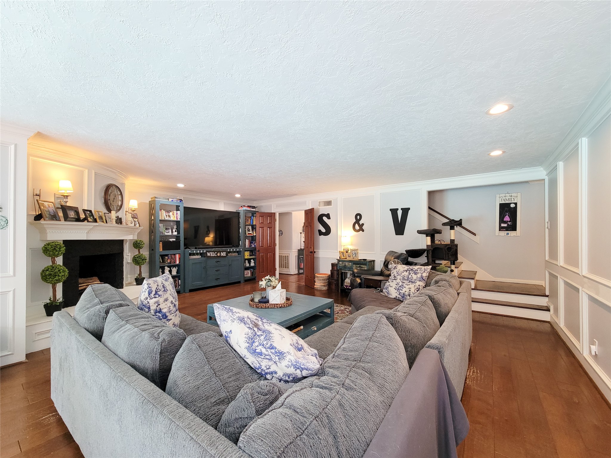 This spacious living room features a cozy sectional sofa, a built-in fireplace, and elegant wood paneling. It includes ample shelving and a TV unit, creating a perfect blend of comfort and functionality.