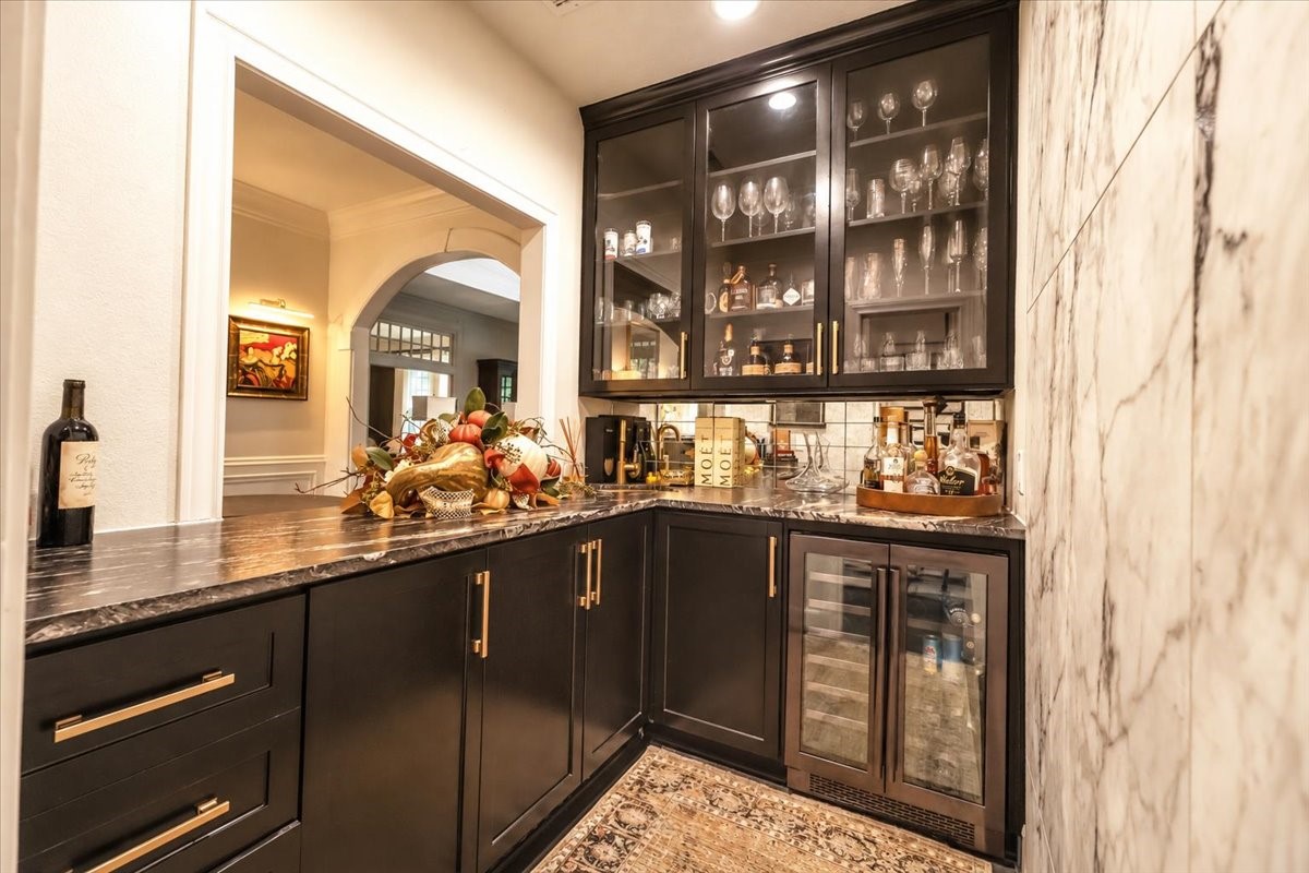 Custom cabinetry with glass fronts, a gold sink, and a leathered-granite waterfall countertop make hosting easy, with a wine fridge beneath for chilled bottles.