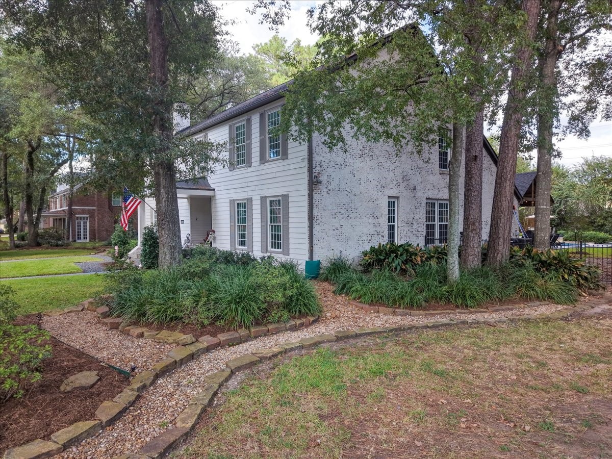 German schmear applied across the brick in 2022 gives the home a soft, refined finish, framed by gray shutters, mature trees, and stone-edged landscape beds.
