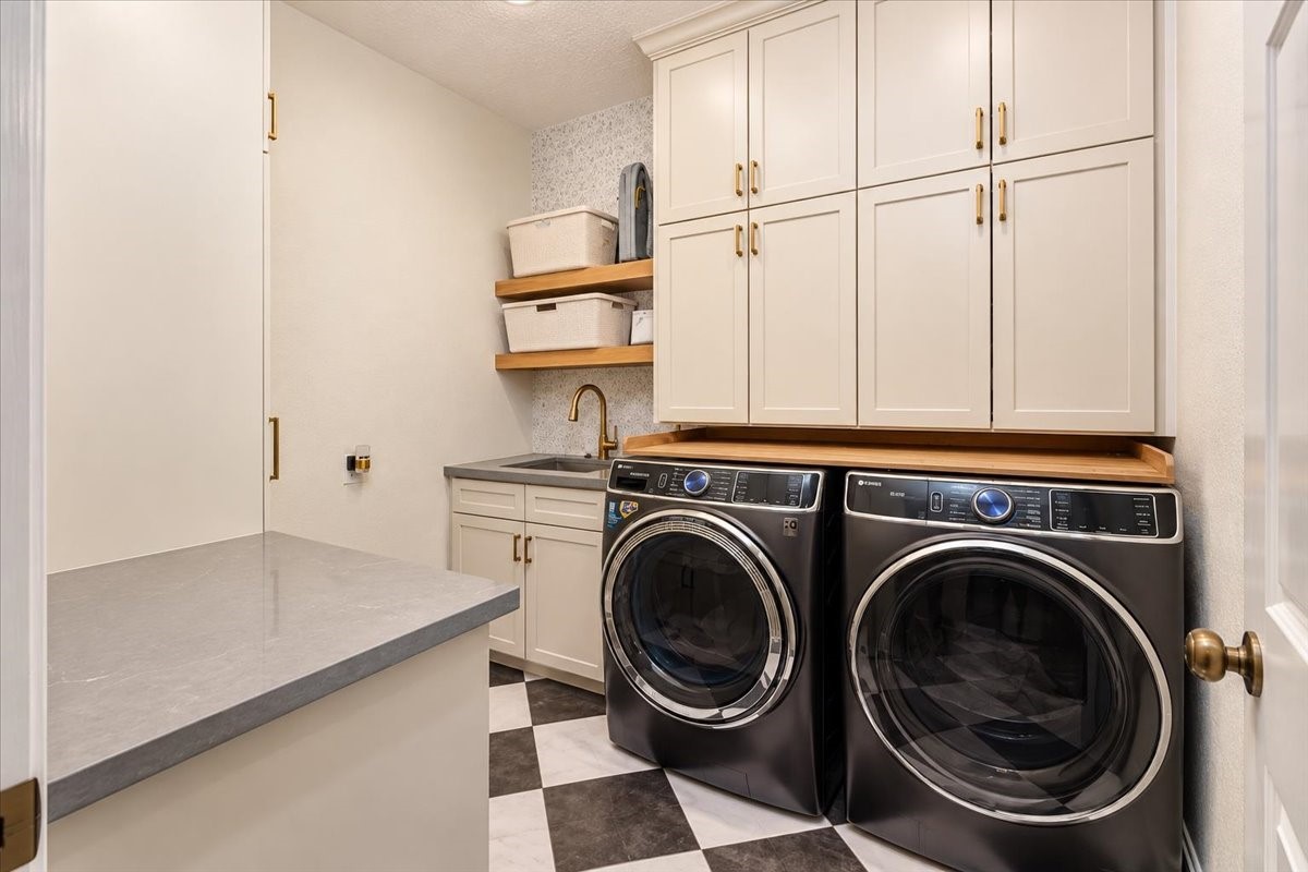 Custom cabinetry with gold hardware, open wood shelves, and a sink with a gold sprayer faucet give this laundry room room for supplies, folding, and everyday routines.