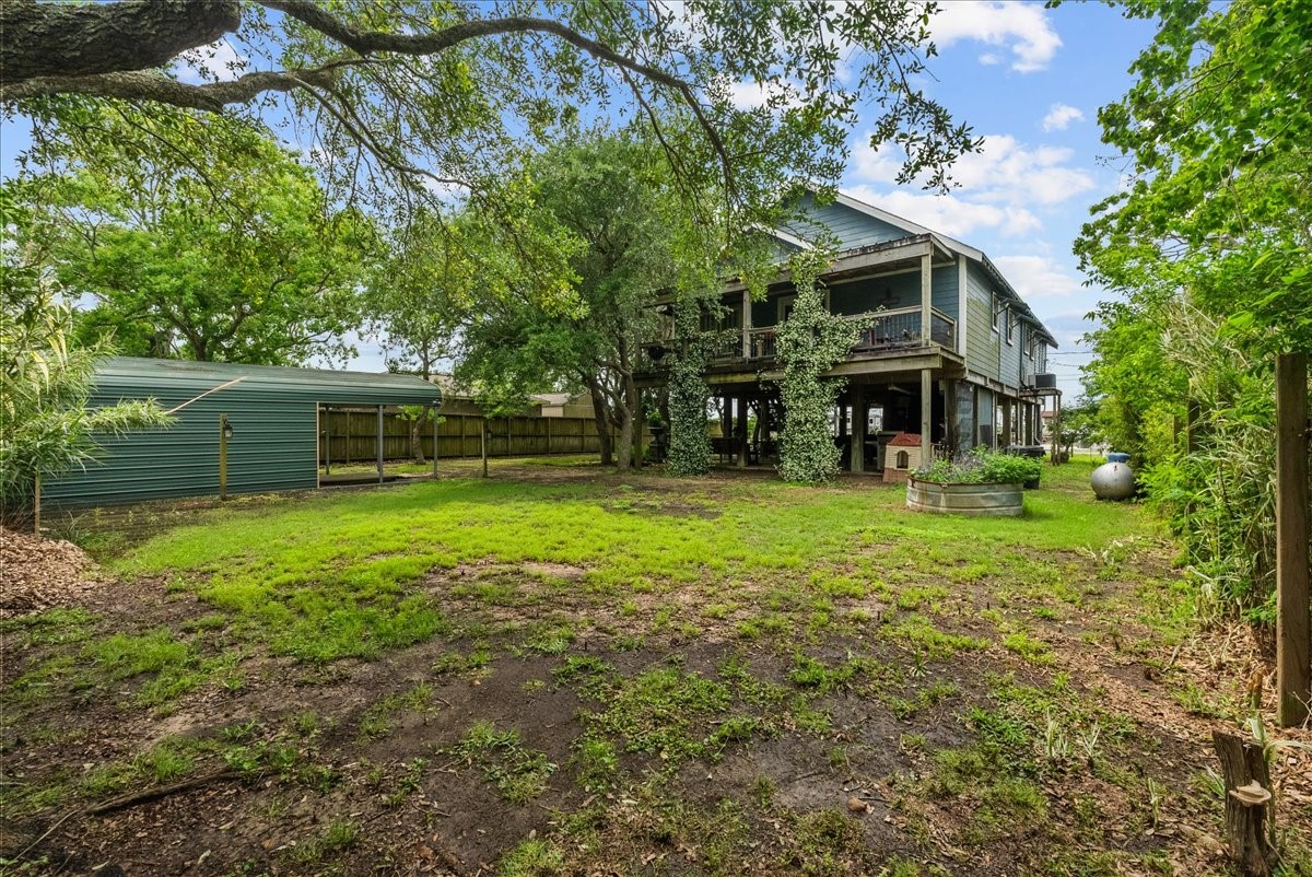 Spacious backyard with mature trees, multiple storage structures and a view of the home's elevated design and covered outdoor areas