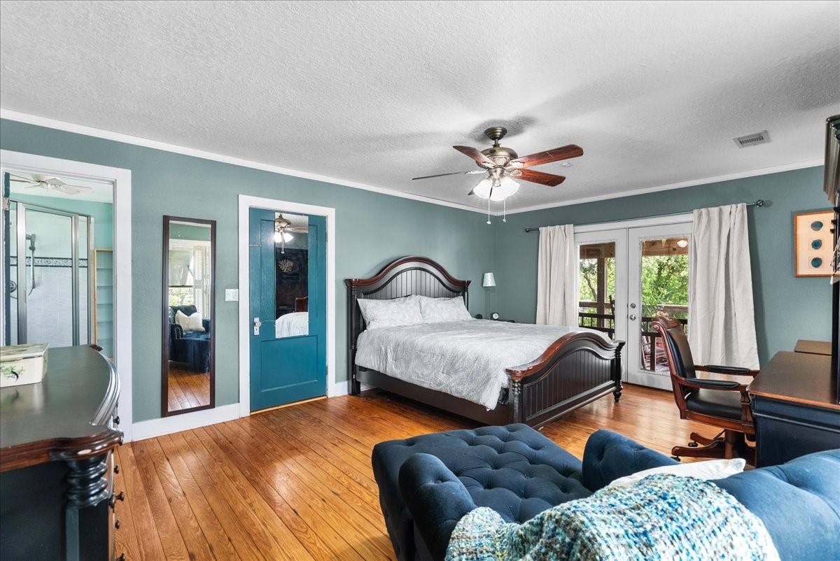 Spacious primary bedroom with hardwood flooring, multiple windows, French doors to the outdoor space and room for an additional sitting or workspace area