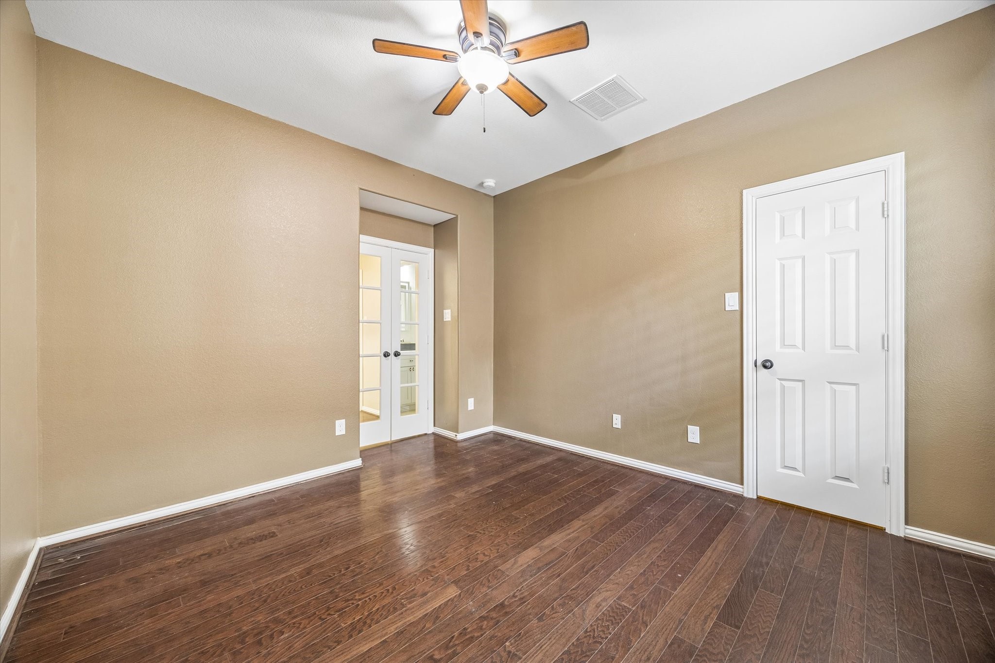 Versatile first-floor study or bedroom featuring wood flooring, double French doors and a ceiling fan, offering flexibility for a home office, guest accommodations or nursery.