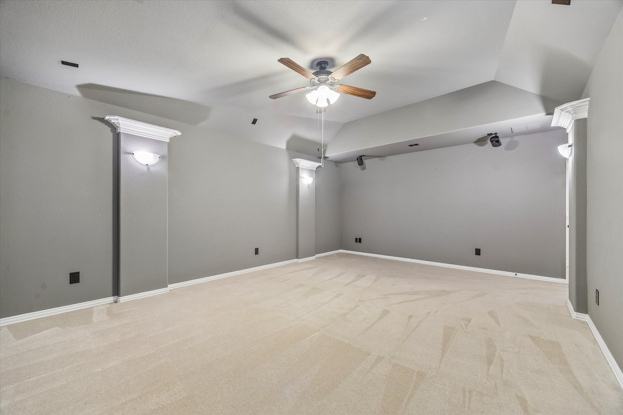Dedicated media room features rich wall tones, decorative columns, wall sconces, and a ceiling fan, creating an inviting setting for movie nights and entertainment.