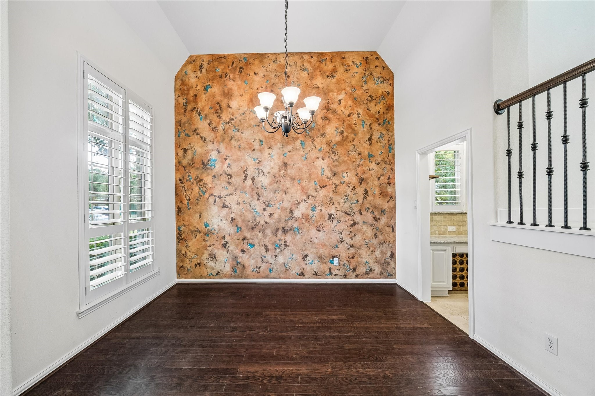 Plantation shutters filter natural light into the dining room, where a high ceiling, wood flooring, and a decorative accent wall provide an inviting setting for gatherings.