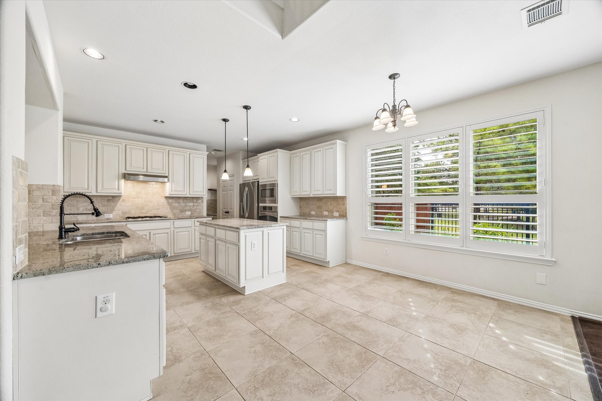 Island kitchen offers abundant white cabinetry, generous counter space and pendant lighting. Adjoining  breakfast area with plantation shutters provides a bright setting for casual dining.