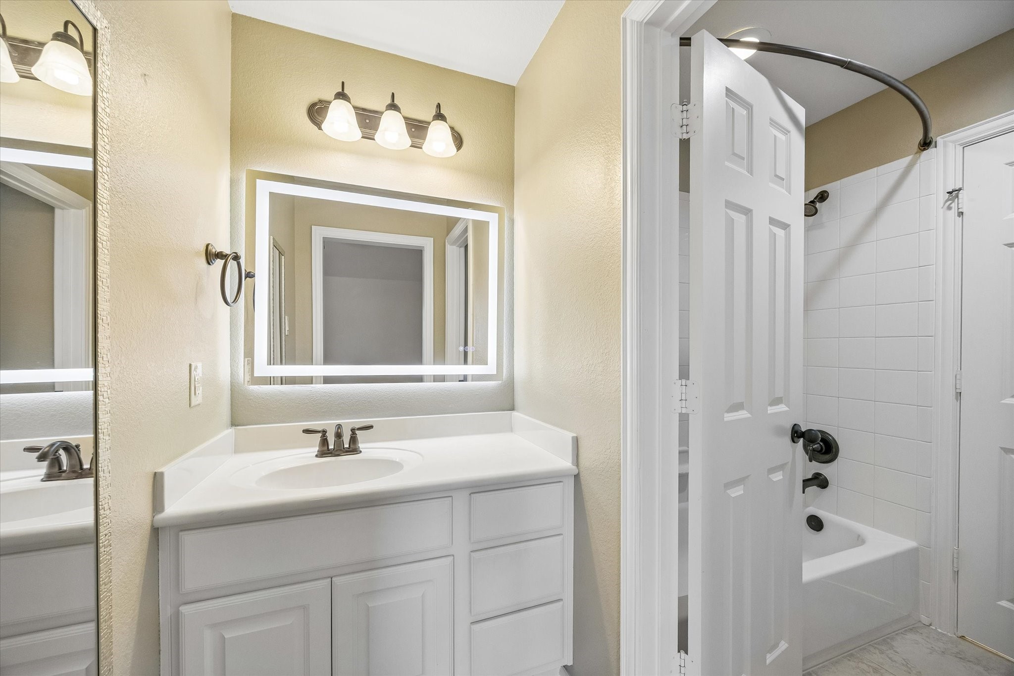 Another view of the Jack-and-Jill bath highlights the separate vanity areas, illuminated mirrors, and shared tub and shower space.