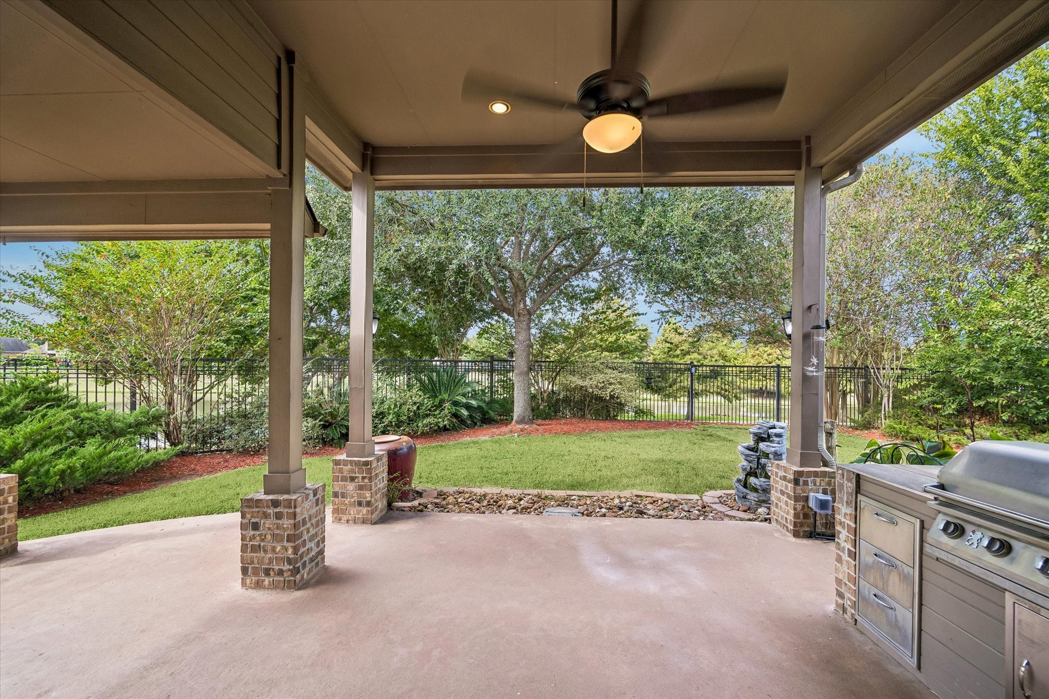 Spacious covered patio features a built-in grill, ceiling fan and brick-accented columns, with room for outdoor dining and lounging overlooking the landscaped backyard and lake.