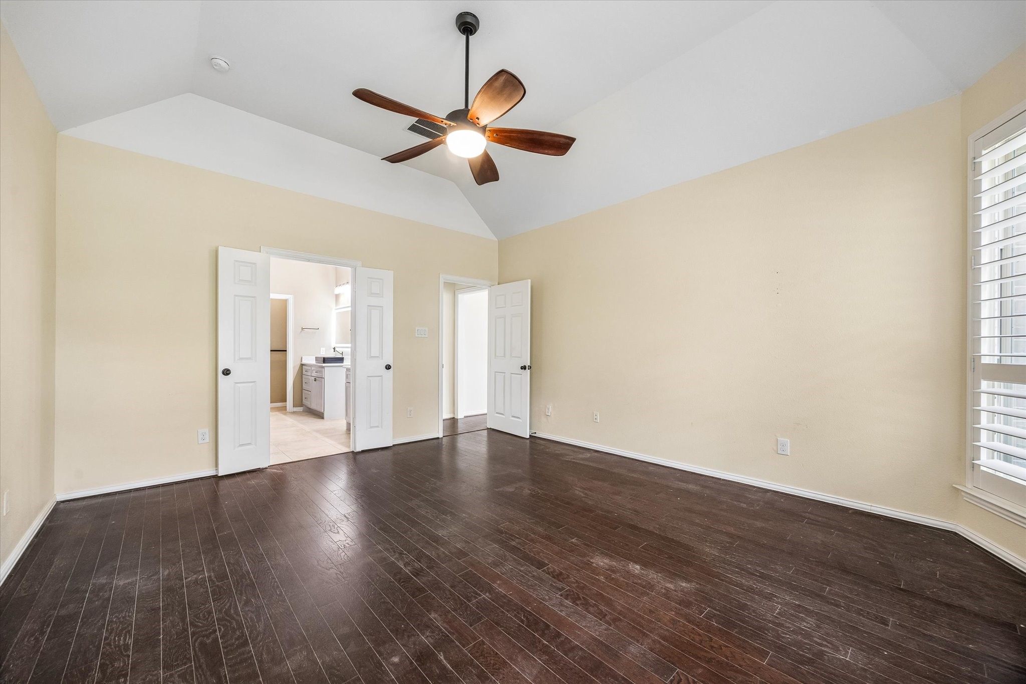 Alternate view of the primary bedroom highlights its generous proportions and vaulted ceiling, with double doors opening to the en-suite bath.