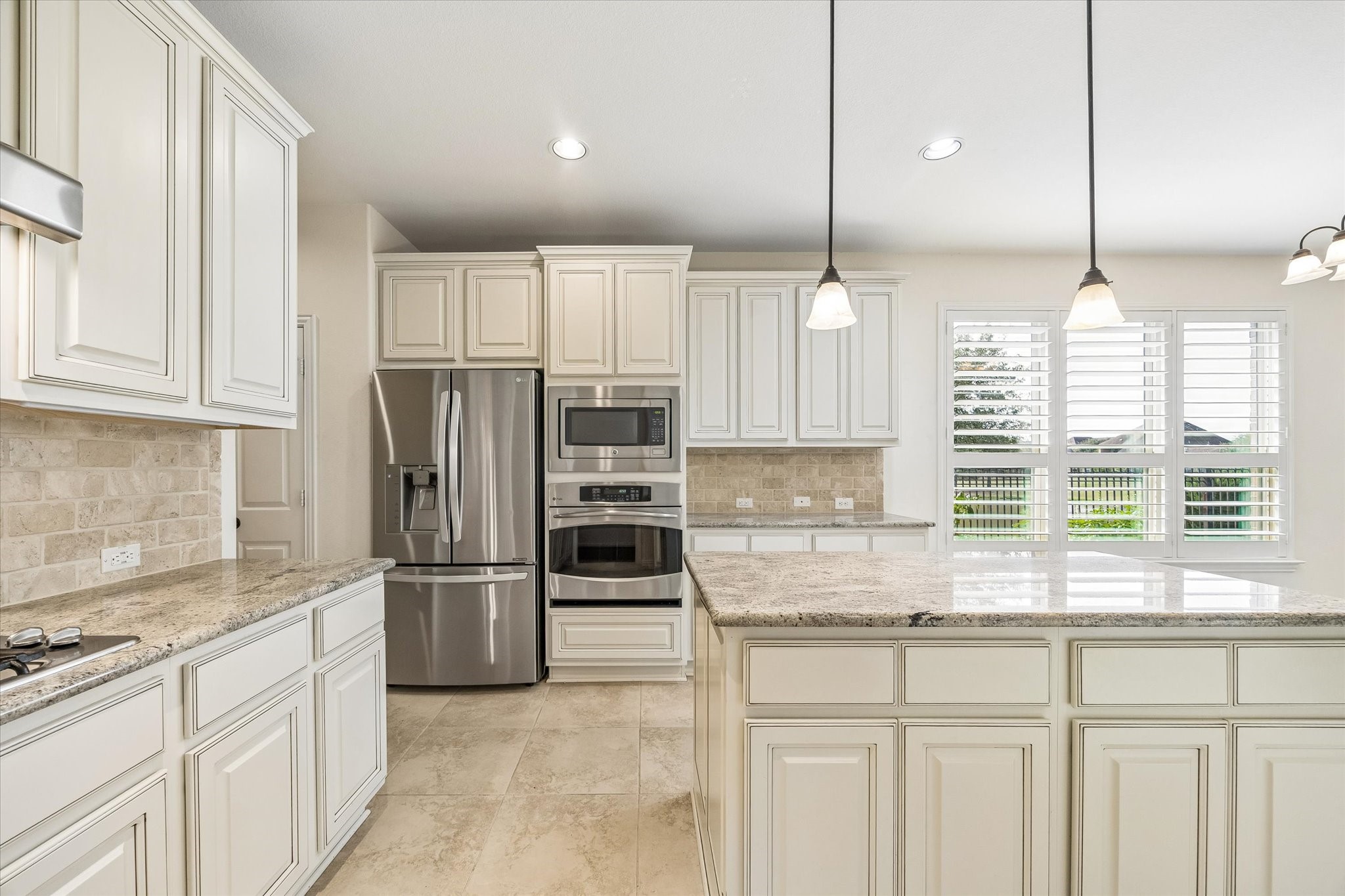 Generous island with built-in storage, neutral tile backsplash and coordinating floors complement the light finishes with the breakfast area just behind.