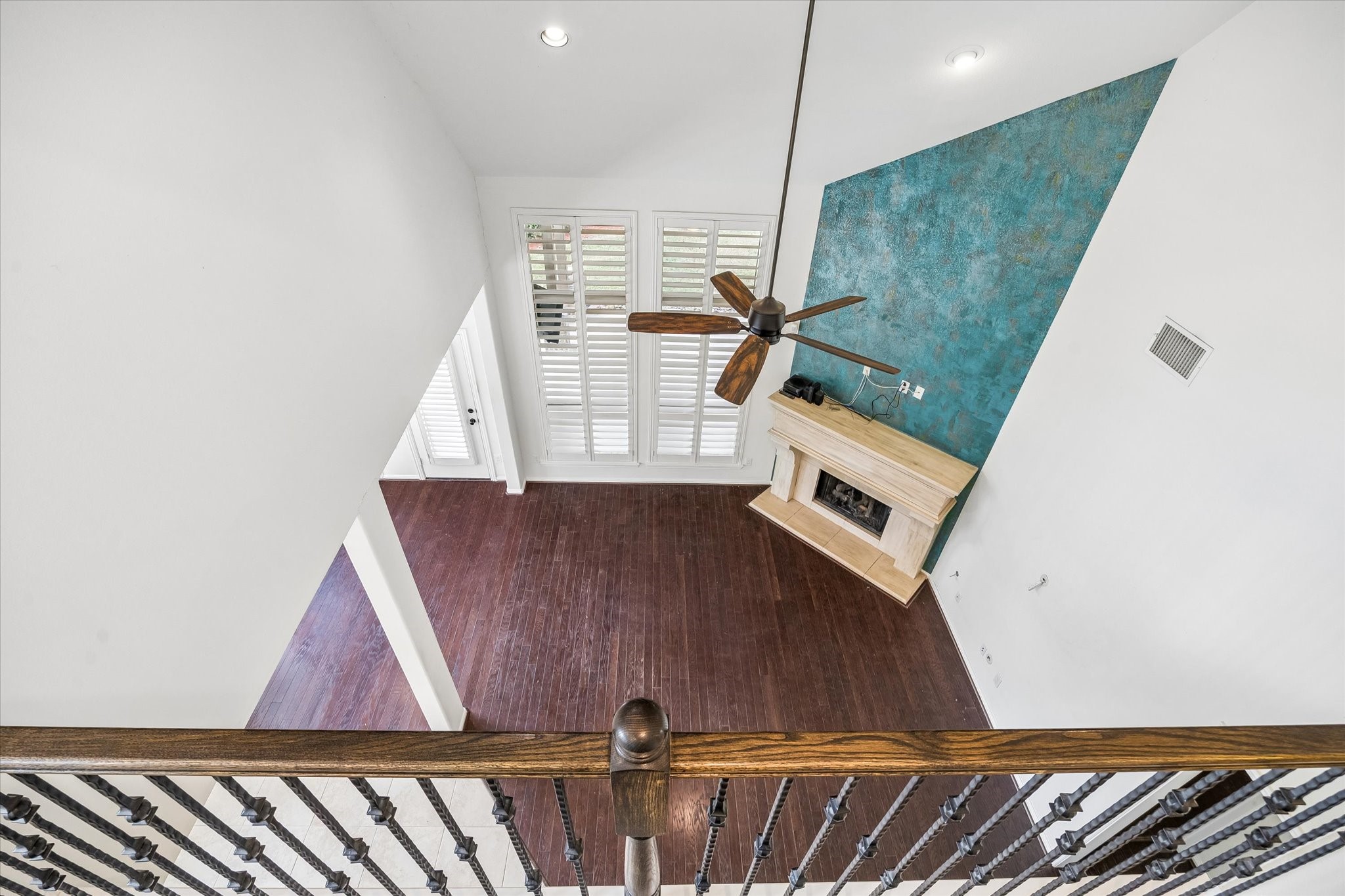 View from the upstairs game room showcases the soaring ceiling, plantation shutters, and striking blue fireplace accent wall in the living area below.